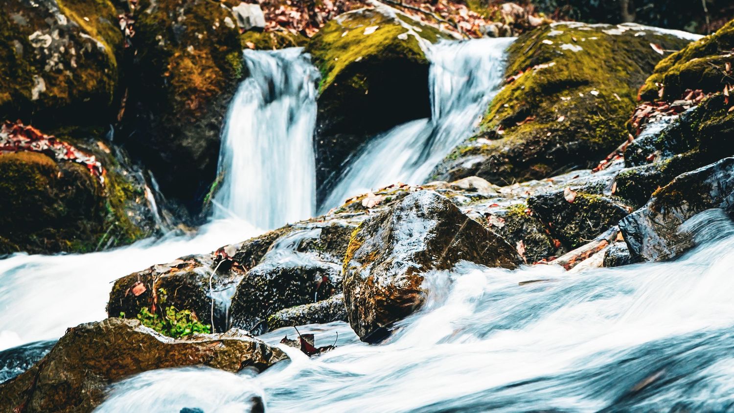 Cascading waterfall flowing over moss-covered rocks in natural setting.