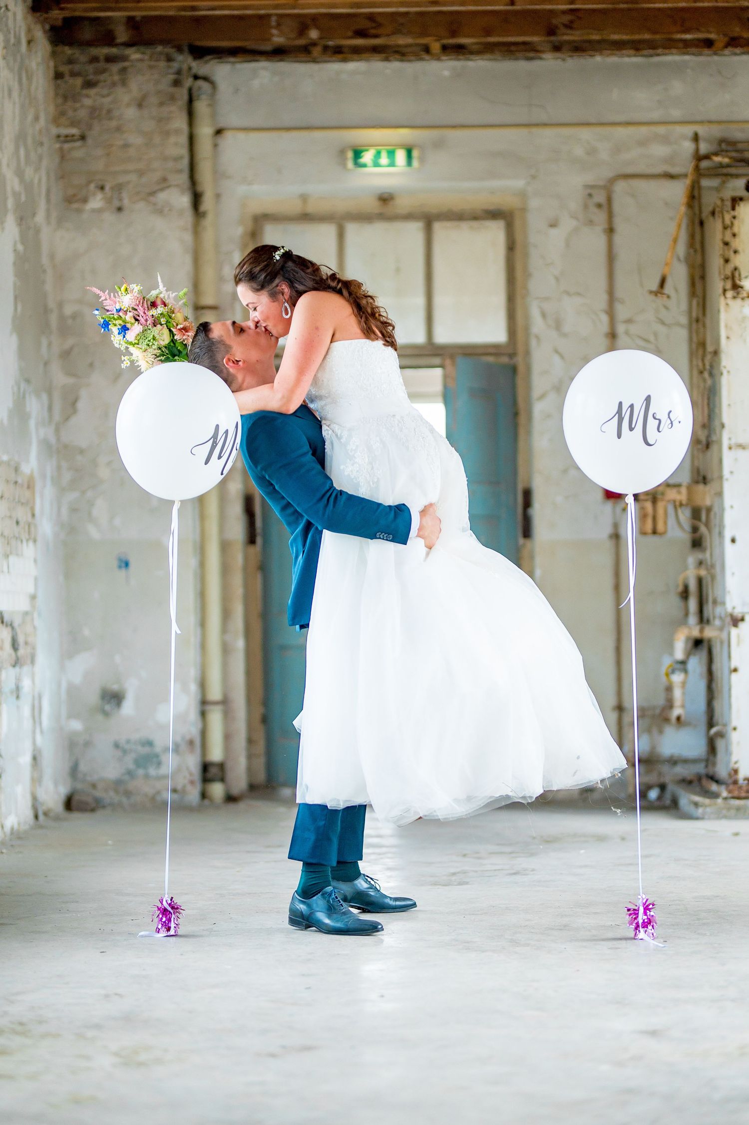 Wedding couple posing in an industrial setting with white balloons and floral decorations.
