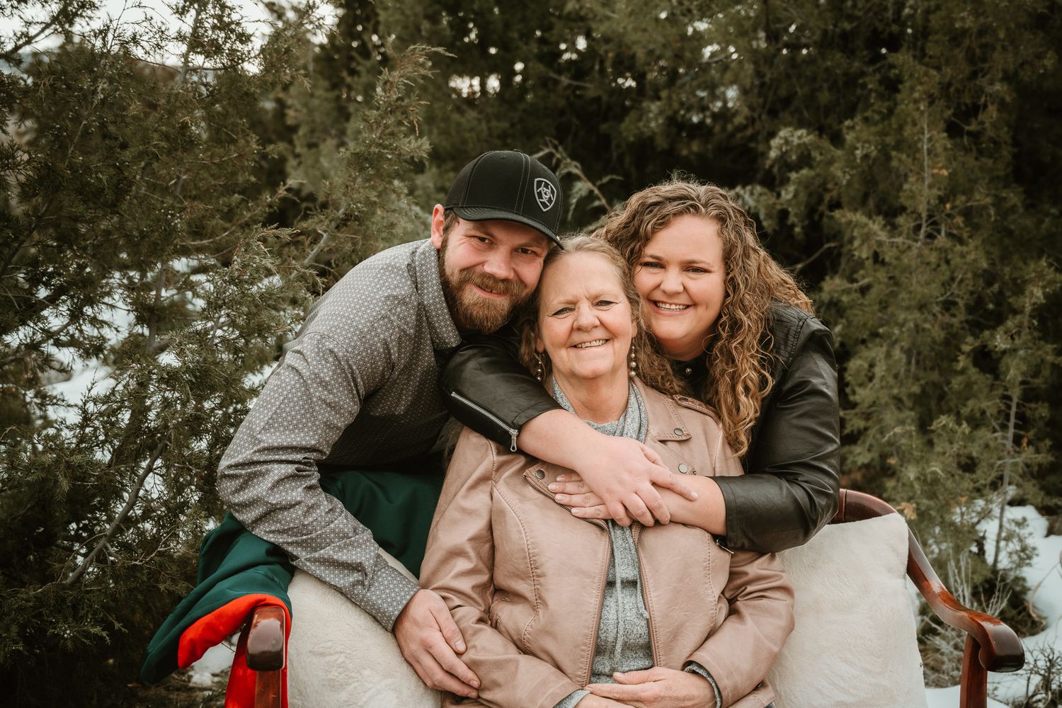 An outdoor winter family photoshoot with snow and evergreen trees in the background.