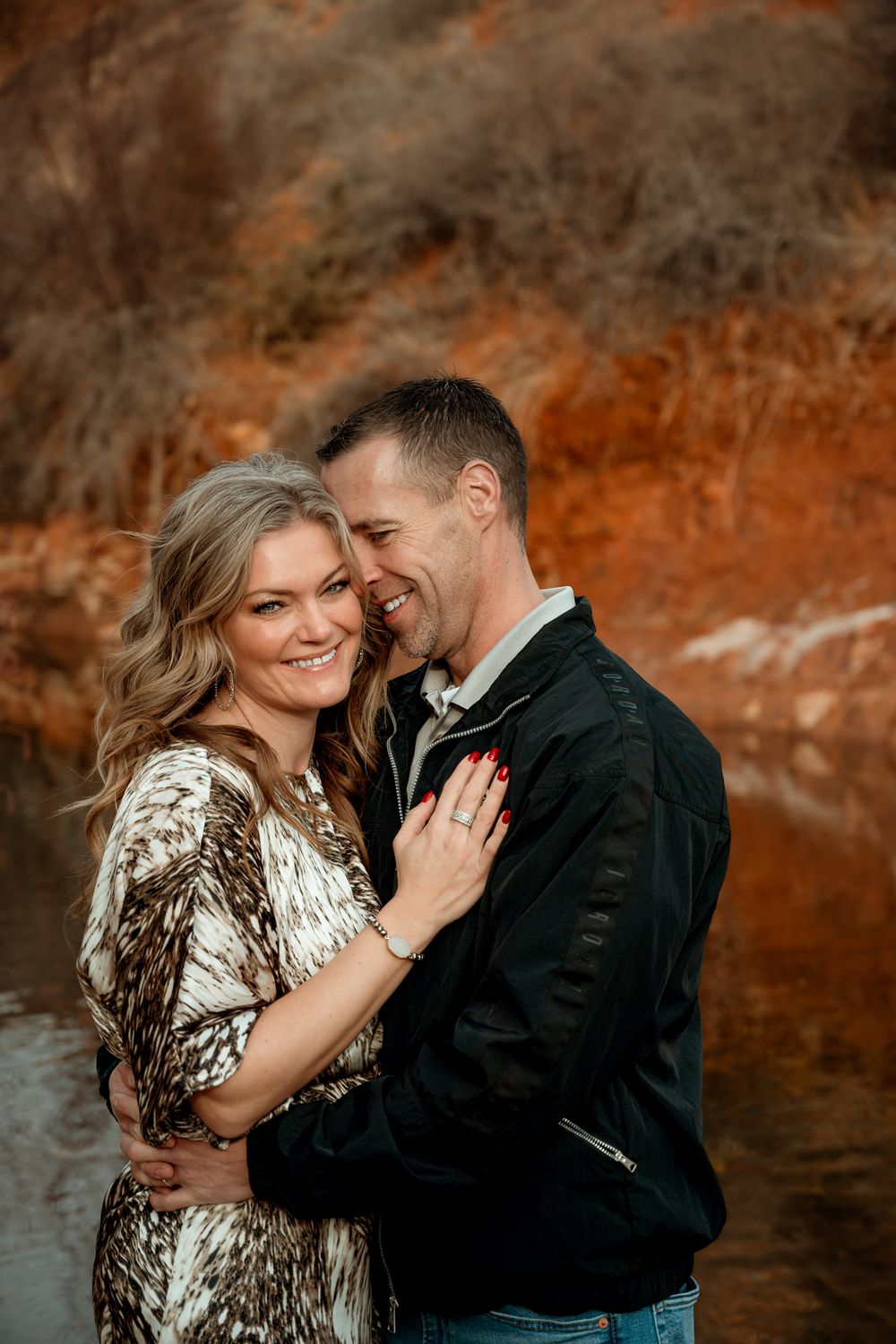 Romantic couple shares an intimate moment against a red rock backdrop at sunset.