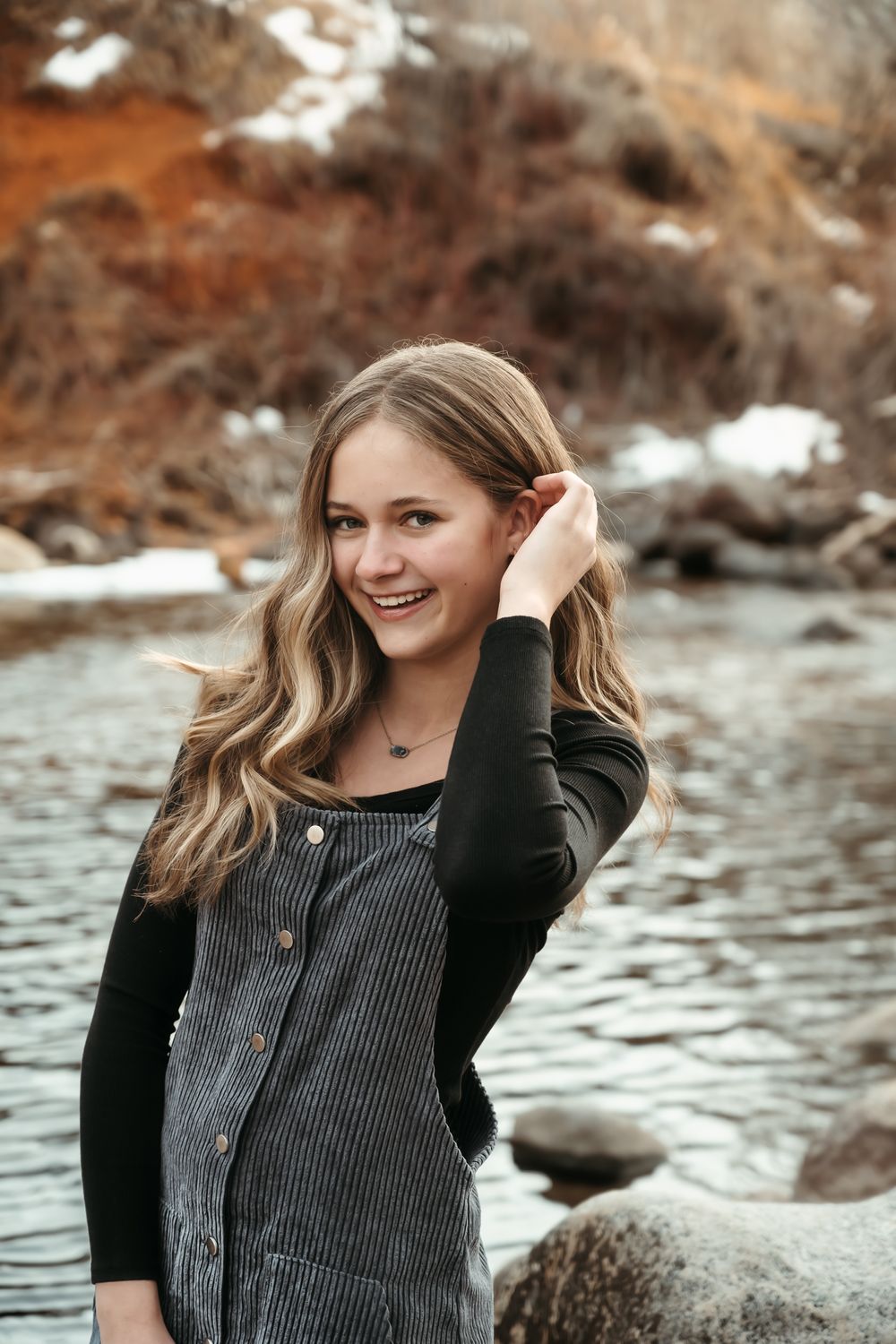 Portrait series in autumn setting by a rocky riverbank wearing grey button-up top.