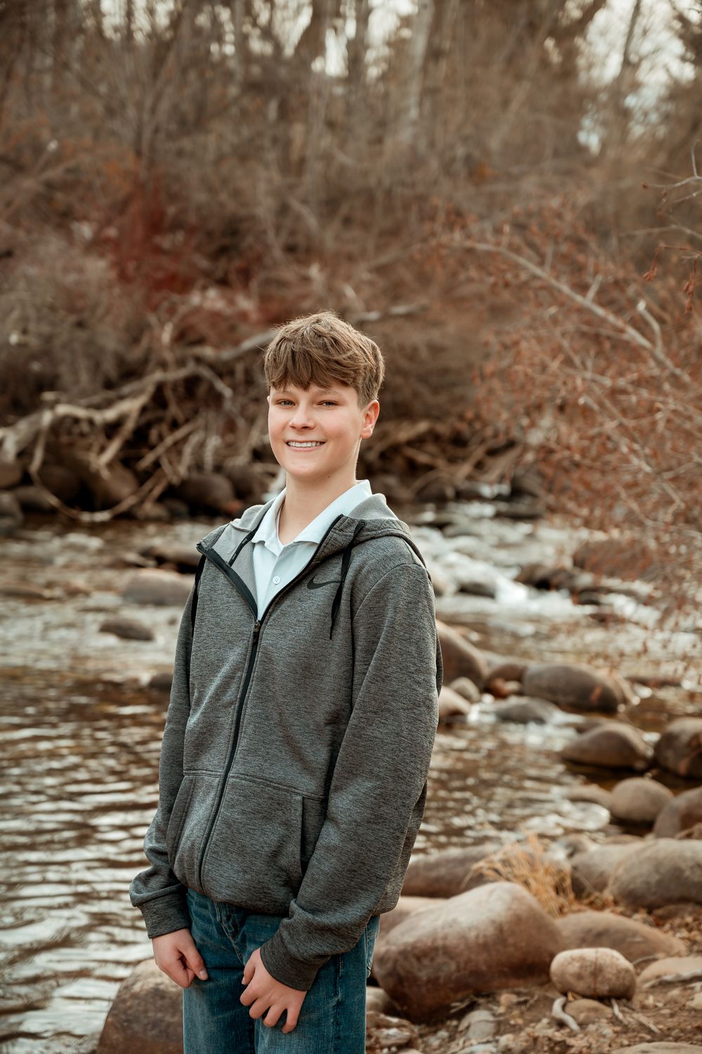 Portrait series by rocky riverbank wearing grey hoodie in autumn setting.