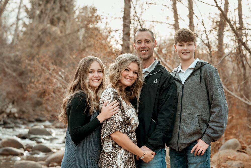 Family photo series by riverside with autumn trees and rocks in background.