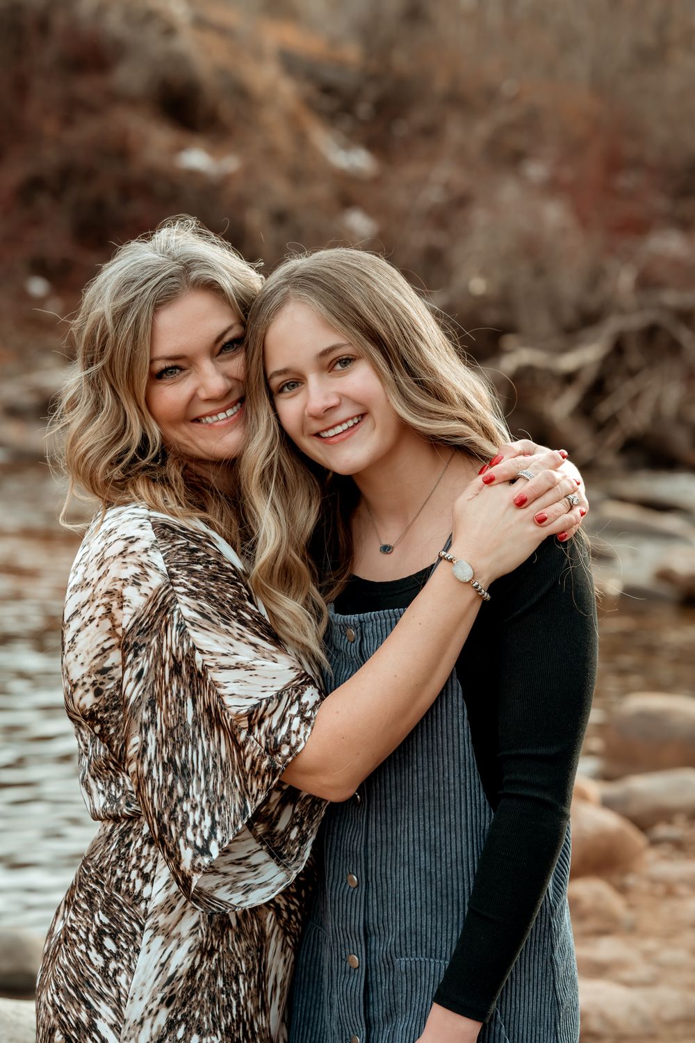 Two people share a warm embrace while sitting on rocky terrain near water.