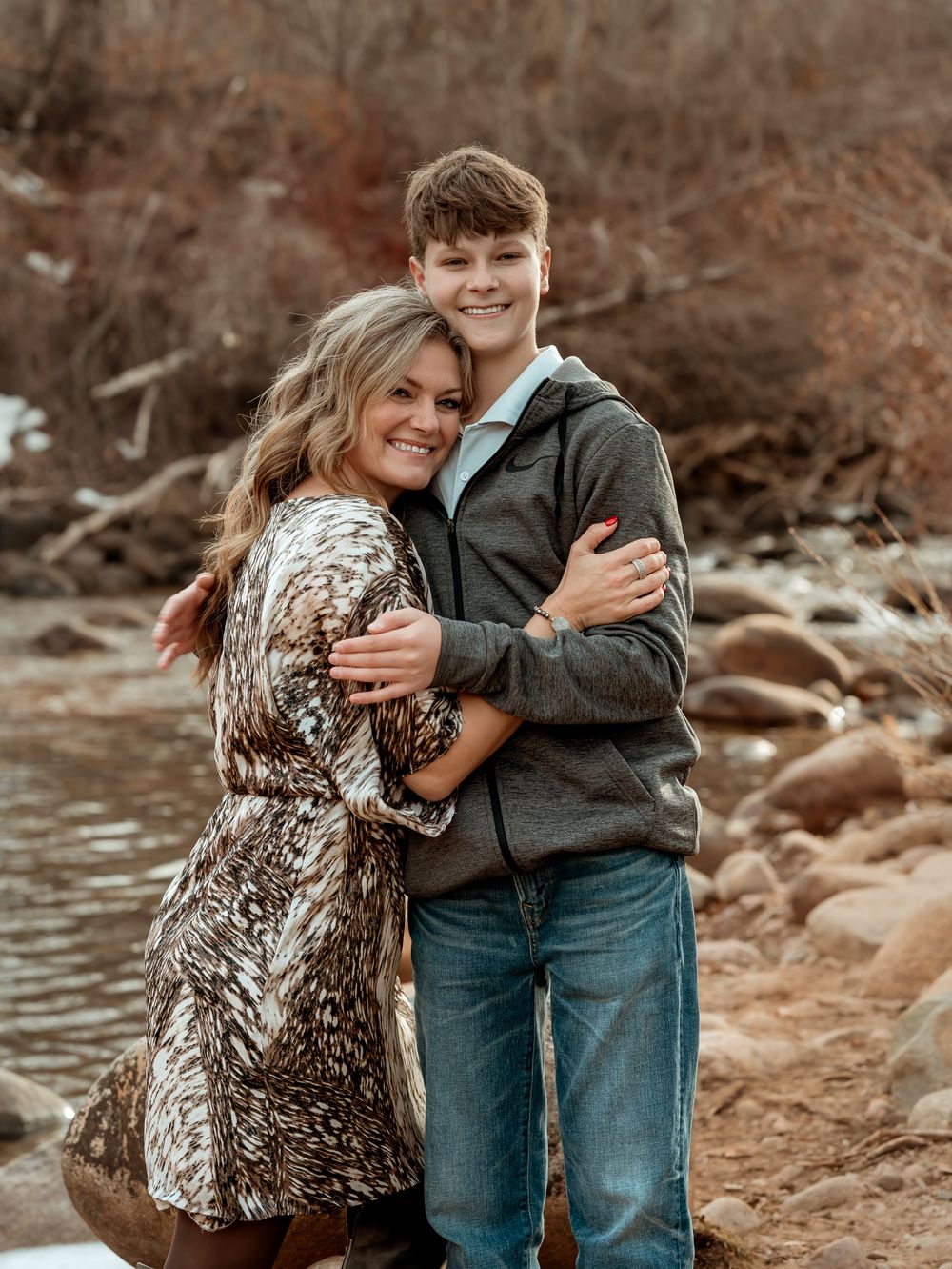 Candid moments captured by a river with rocks and autumn foliage in the background.