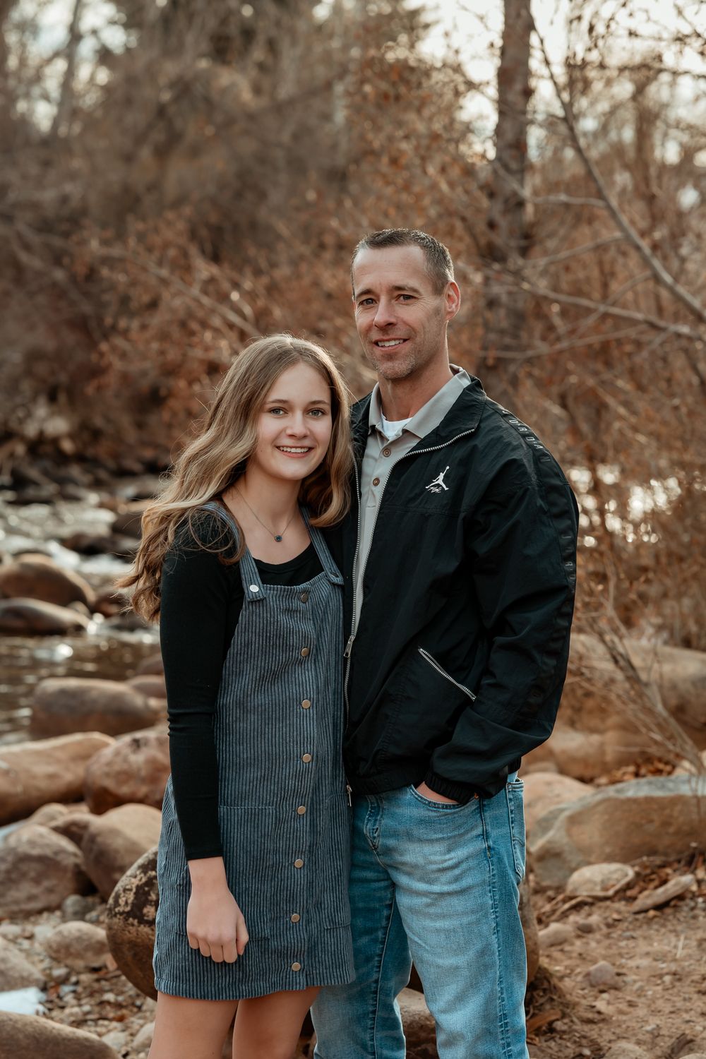 Family portraits by rocky riverbank with autumn foliage in background.