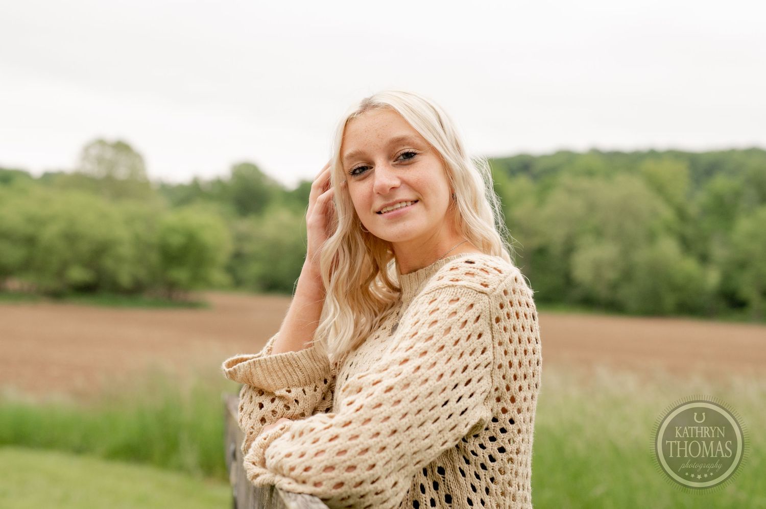 Countryside portrait in cream knit sweater against rolling hills and green landscape.