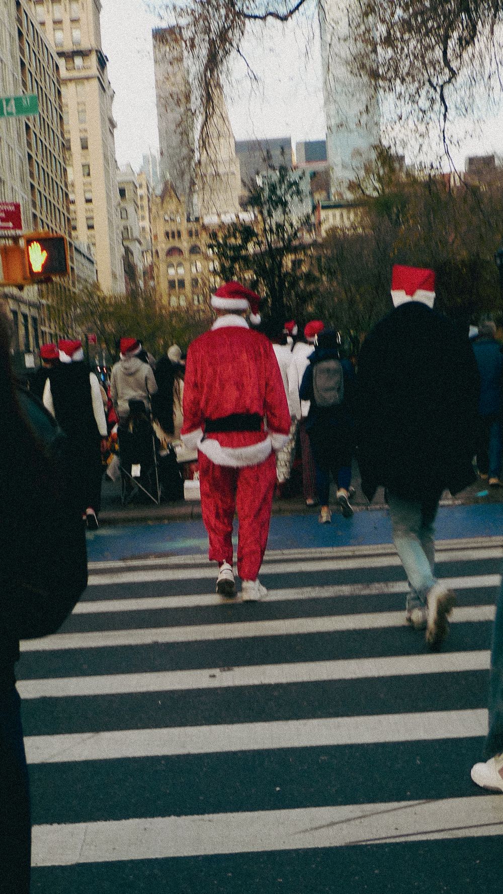 A festive Santa Claus crosses a busy city crosswalk in New York City during the holiday season.