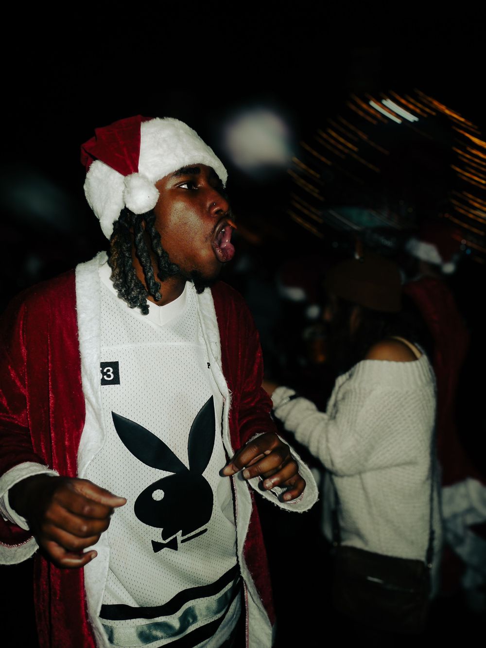 A person wearing a Santa hat and Playboy bunny shirt performs energetically at a nighttime event.