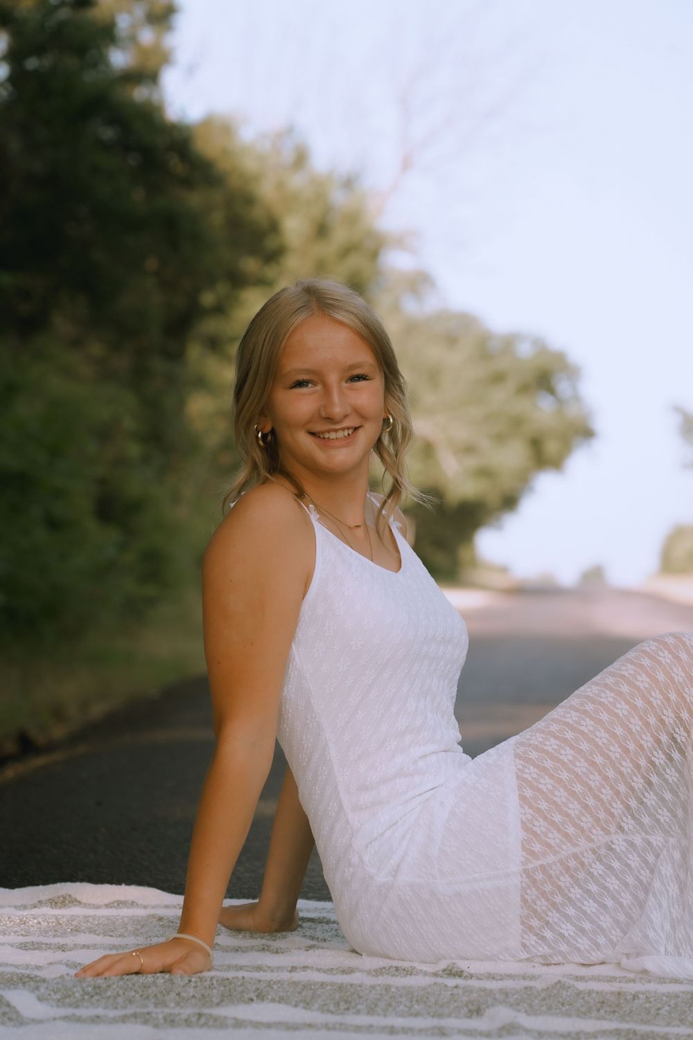 Portrait of someone in a white dress sitting on a blanket outdoors.