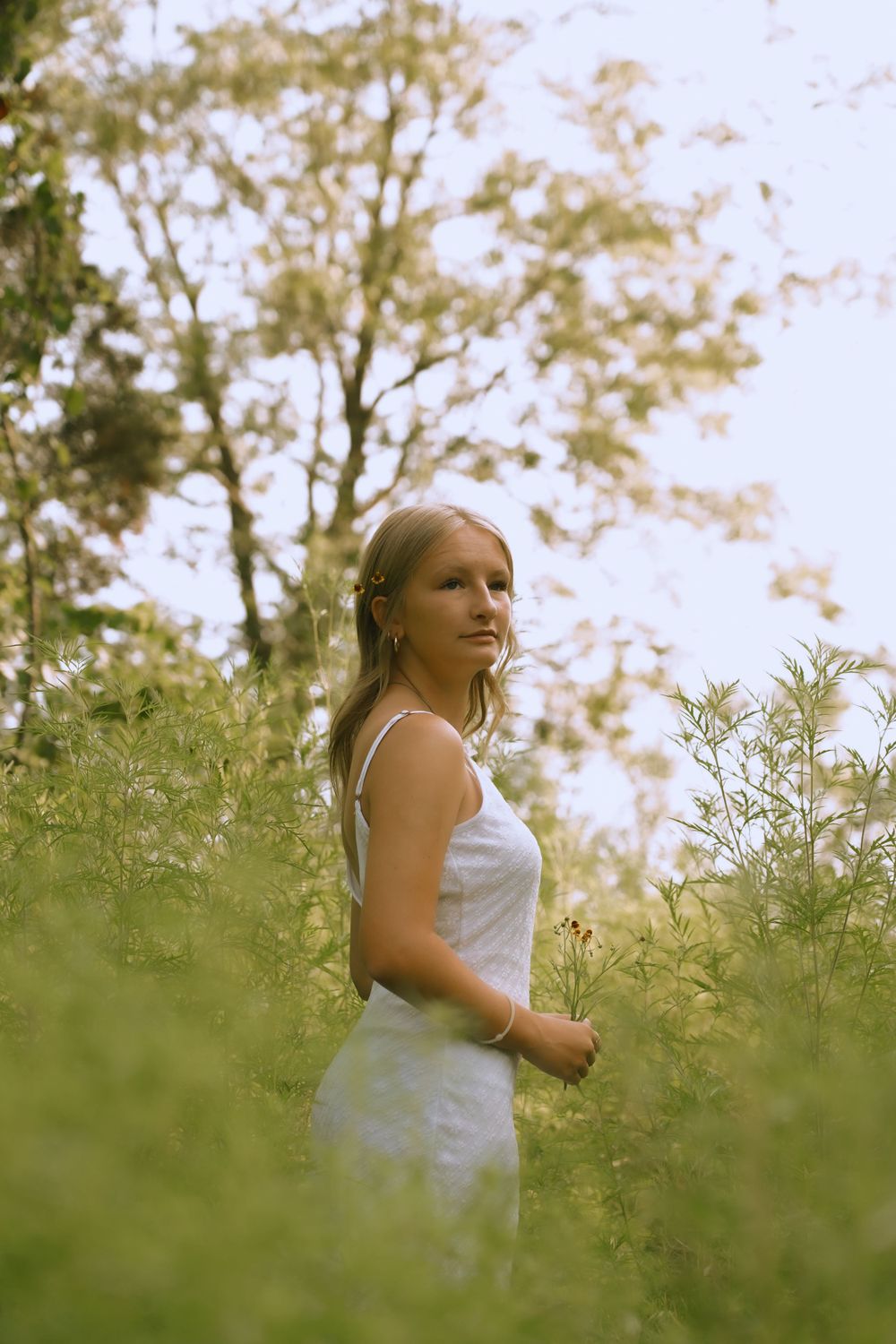 Artistic portrait of someone in a white dress among wild summer grasses.