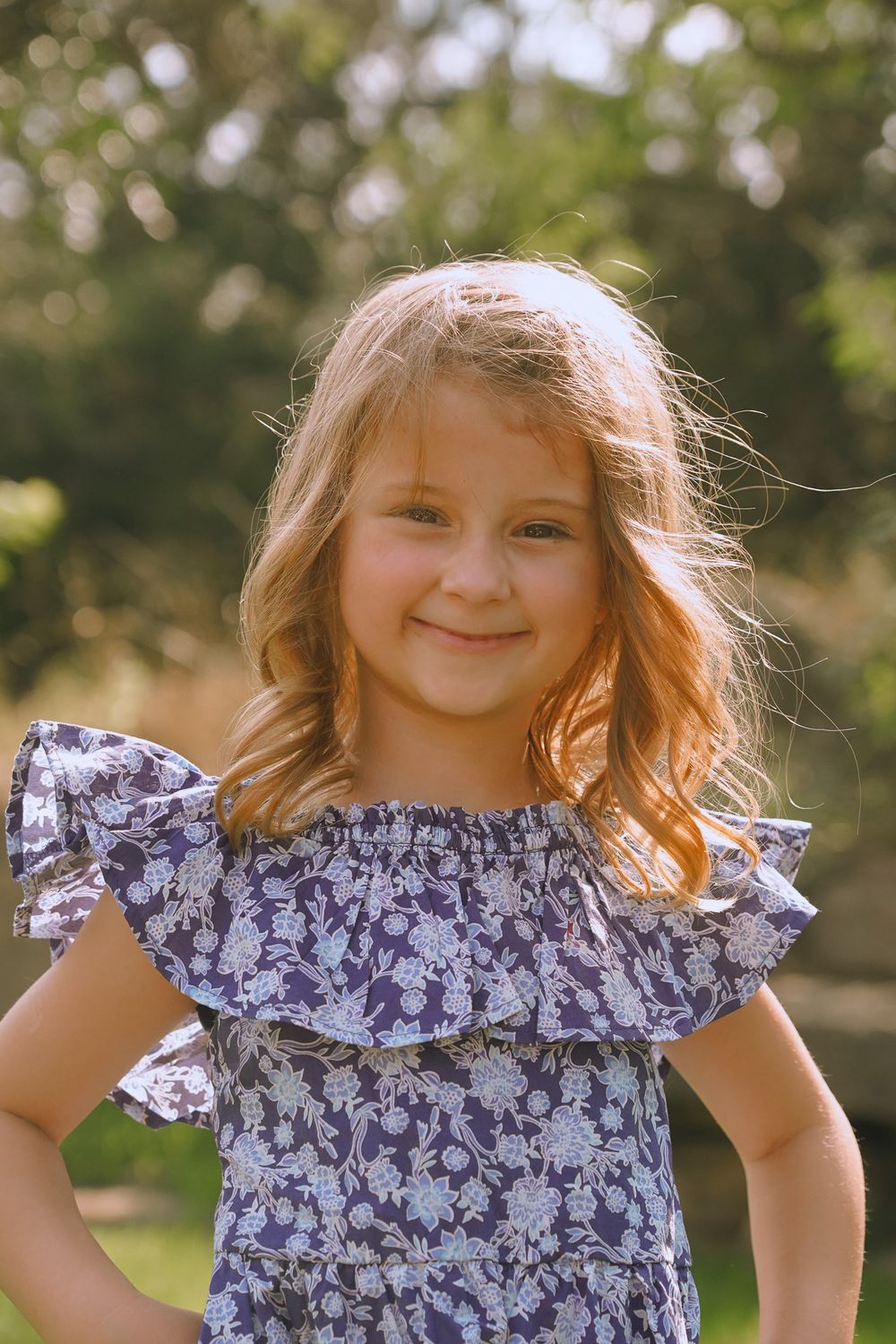 Young person in floral ruffled dress poses outdoors in natural lighting.