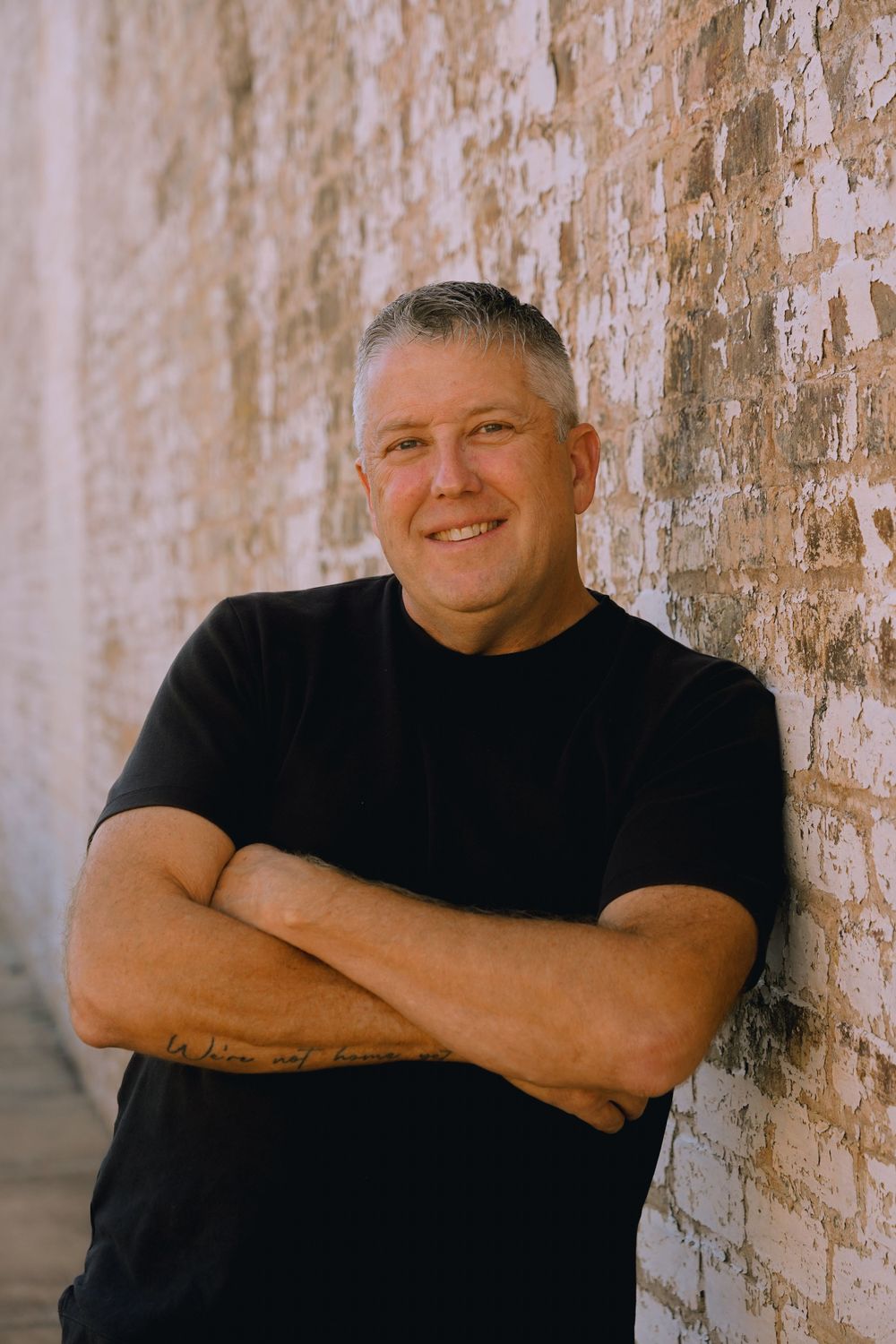 Person in black t-shirt poses against weathered brick wall.