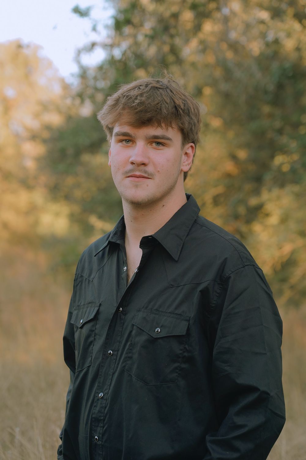 Portrait of someone in a dark button-up shirt against a backdrop of fall colors.