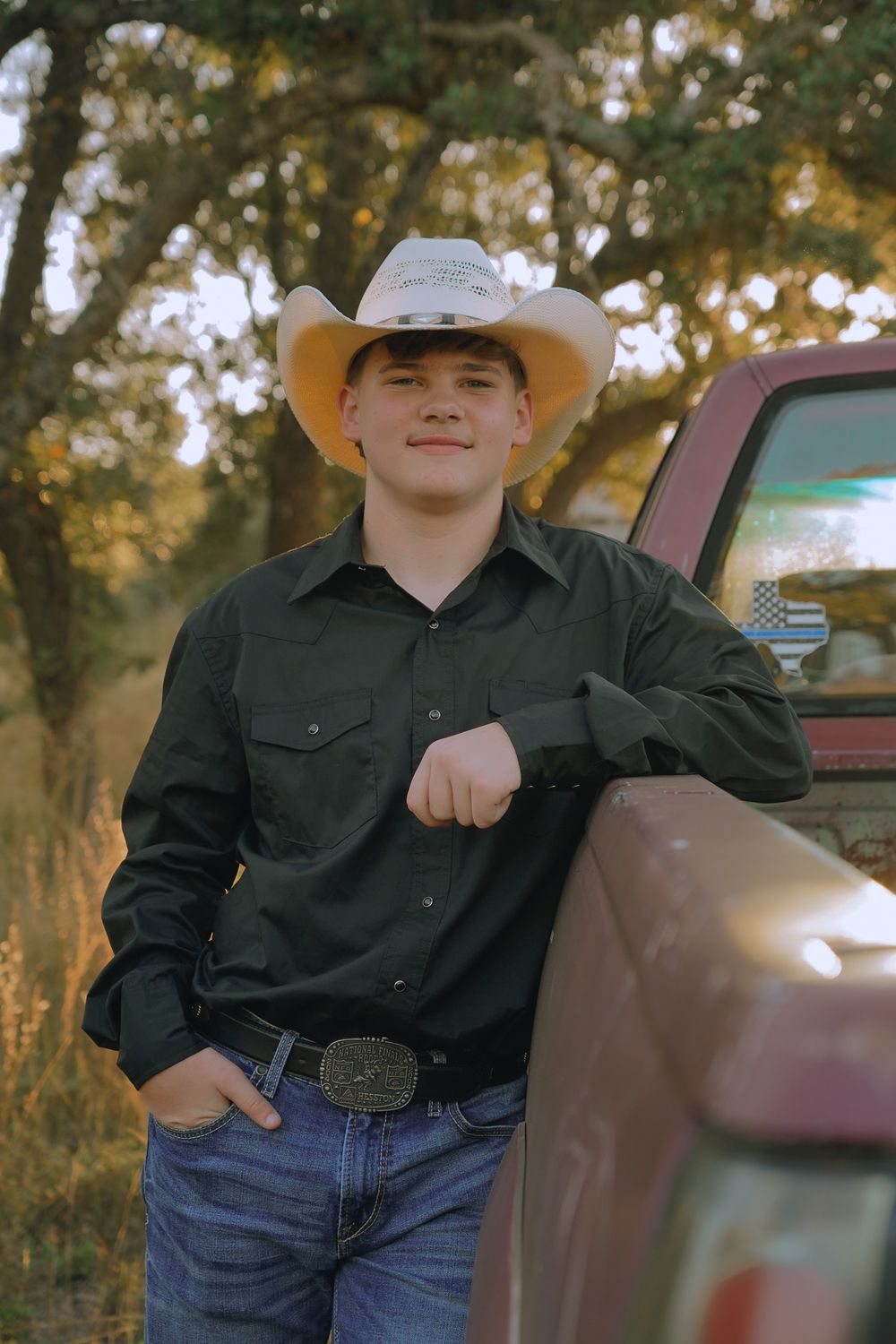 Western-styled portrait of someone leaning against a red truck wearing a cowboy hat.