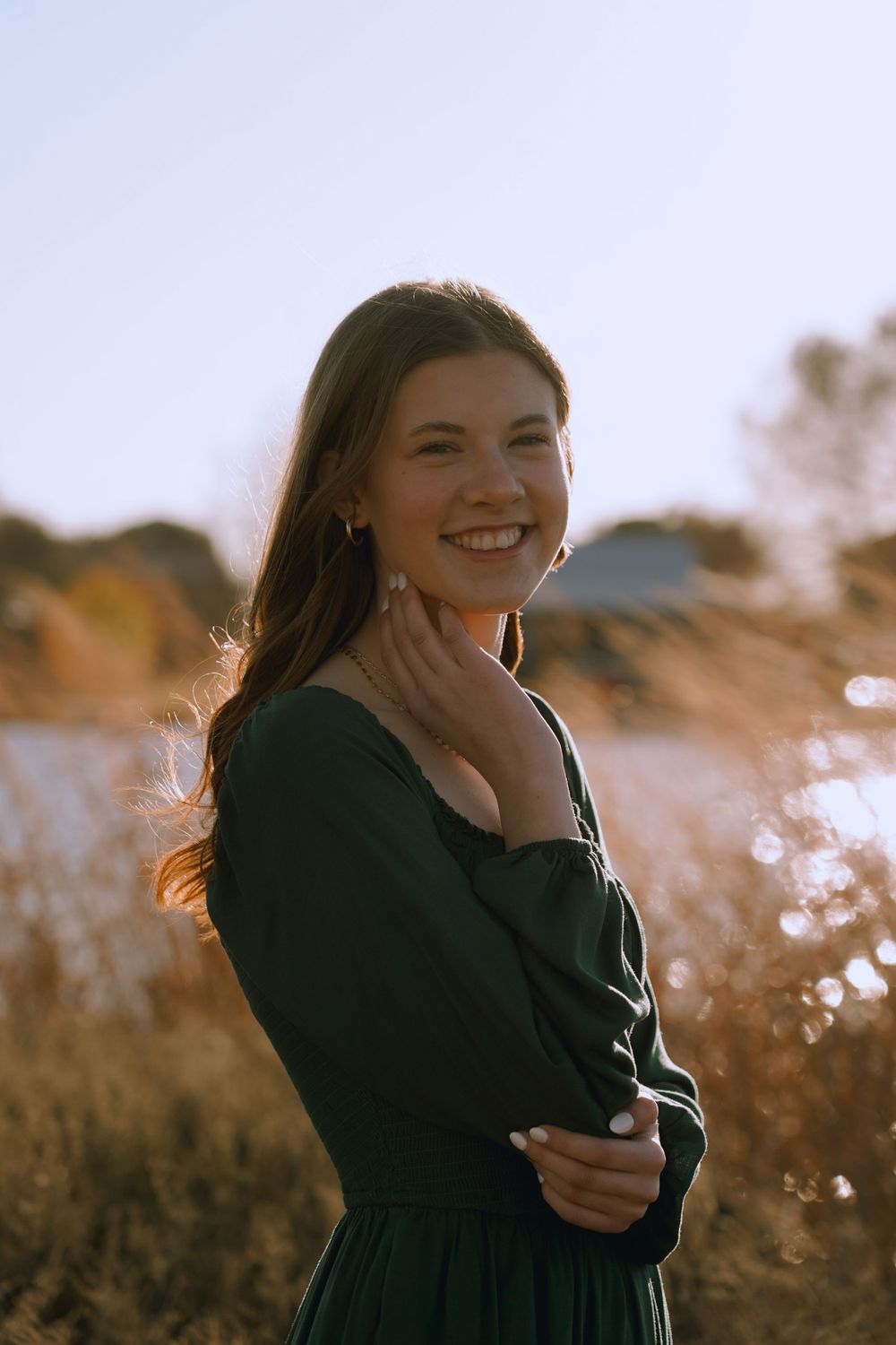 Sunset portrait in nature wearing dark green dress with soft golden light in tall grass field.