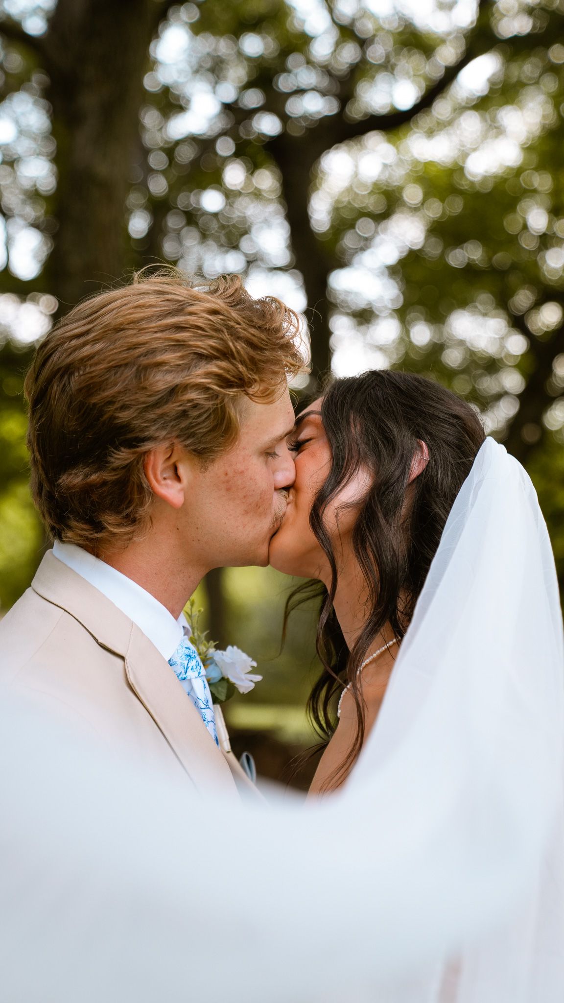 Multiple hands with wedding rings embrace over a white lace wedding dress.