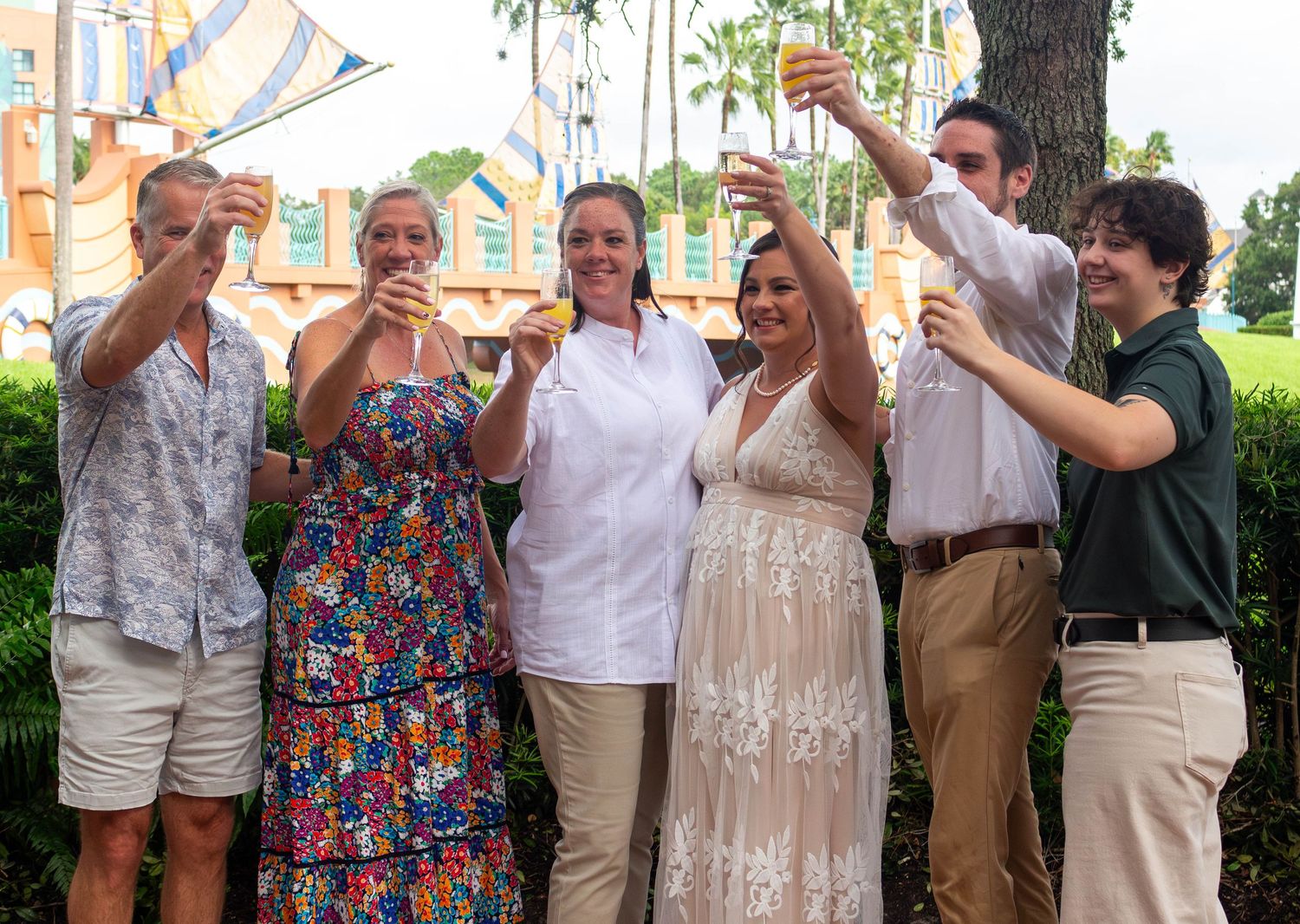A group raises glasses in celebration outdoors by a playground on a sunny day.