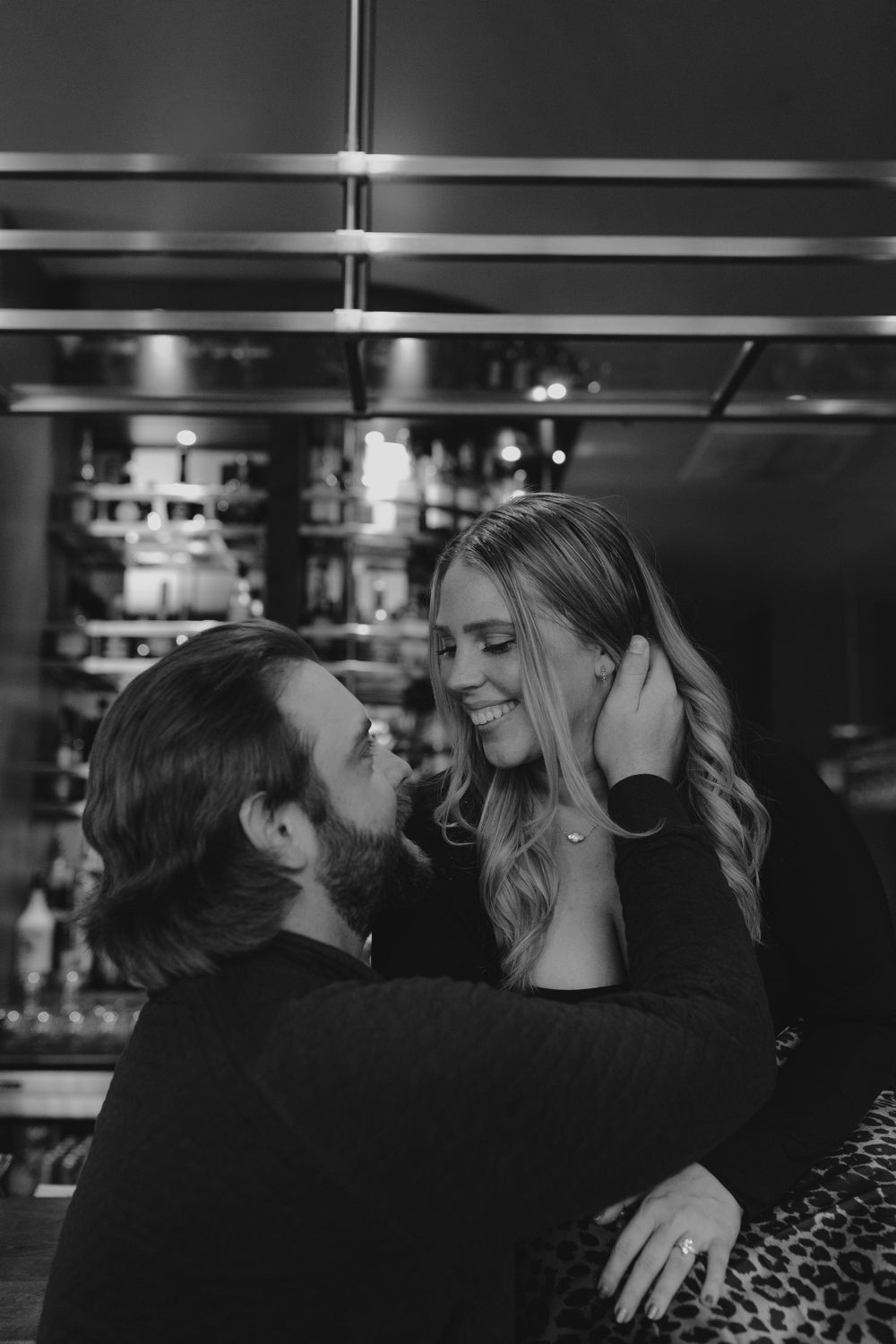 A romantic black and white moment of a couple sharing an intimate embrace at a dimly lit bar.
