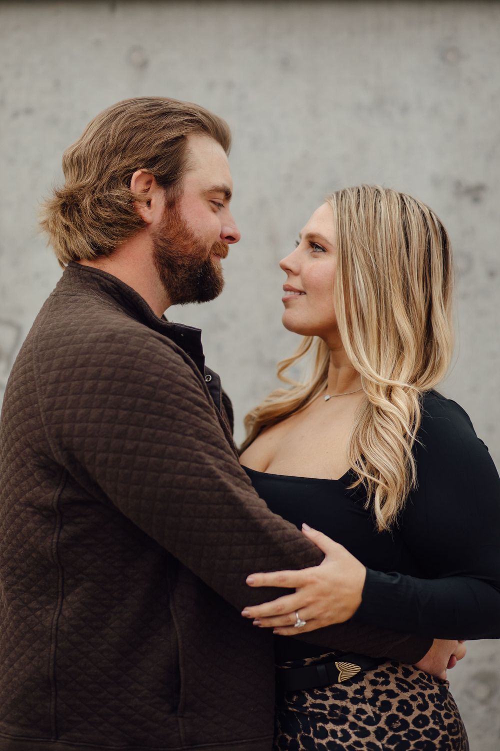 Romantic couple embracing outdoors with the woman wearing a leopard print skirt and man in brown sweater.