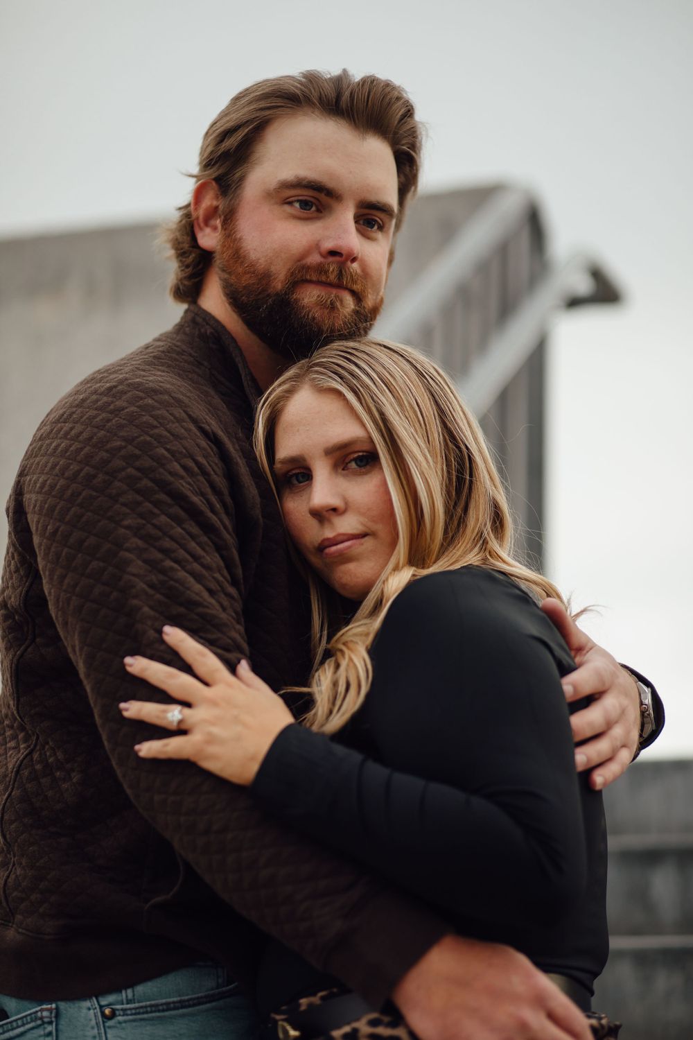 Couple in dark sweaters embrace intimately during outdoor photoshoot with moody, romantic lighting.