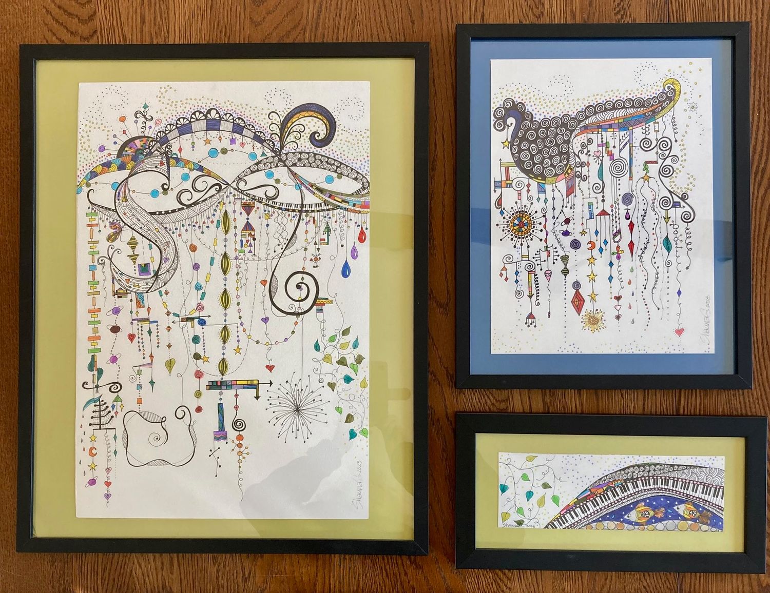 Abstract art featuring swirling patterns with dangling ornaments and decorative elements in two framed pieces.