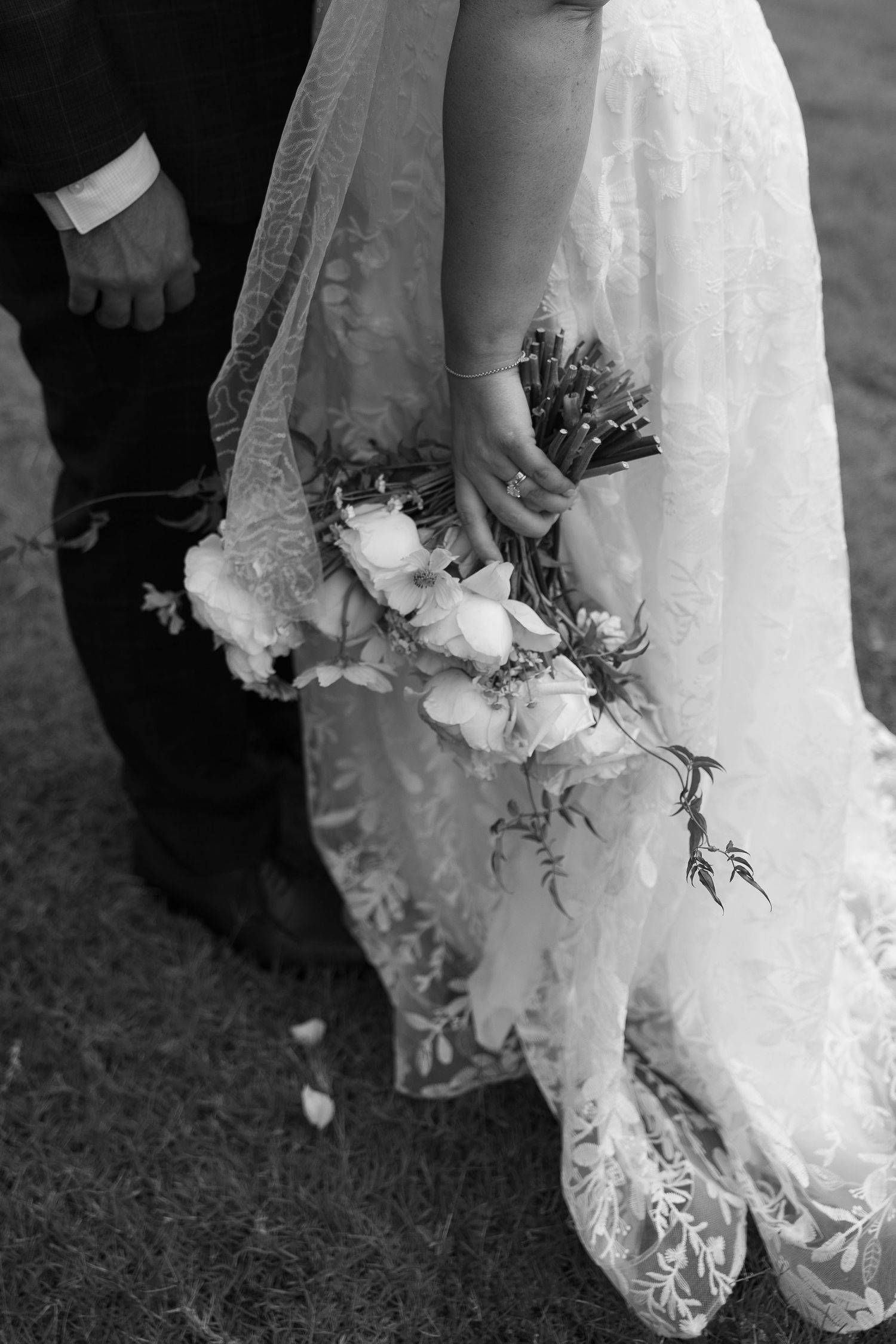 Detail shot of wedding dress hem and bouquet against grass in black and white.