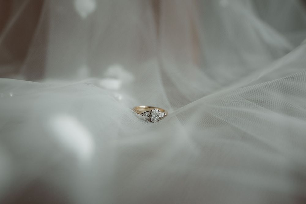 Elegant diamond engagement ring rests delicately on soft white tulle fabric with dreamy lighting effect.