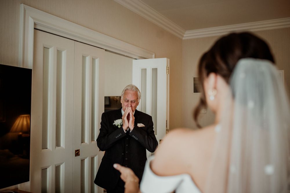 An emotional moment captured as someone in a black suit reacts to seeing a bride in her wedding dress and veil.