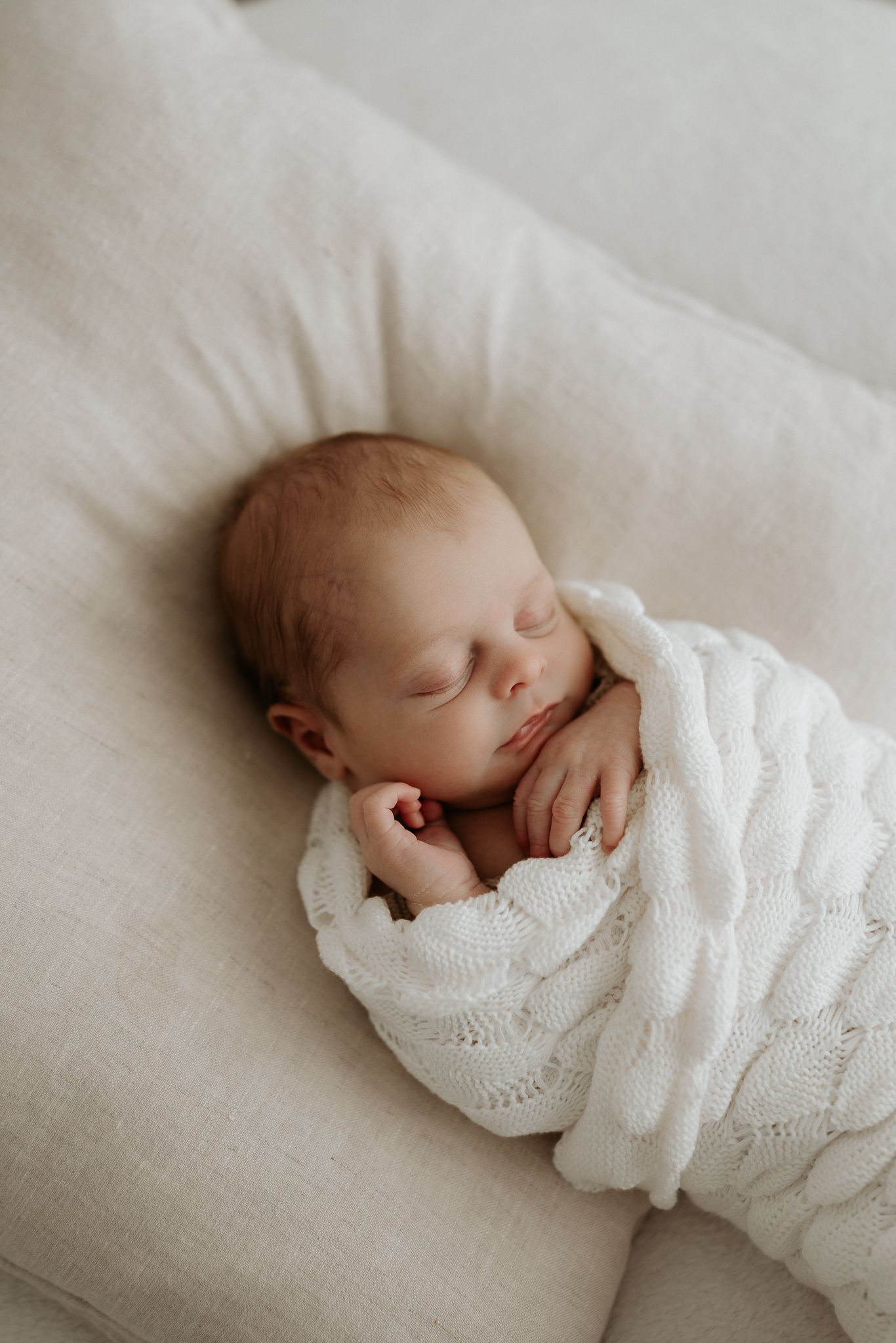 Tender moment with newborn baby cradled in parent's arms on white fabric.