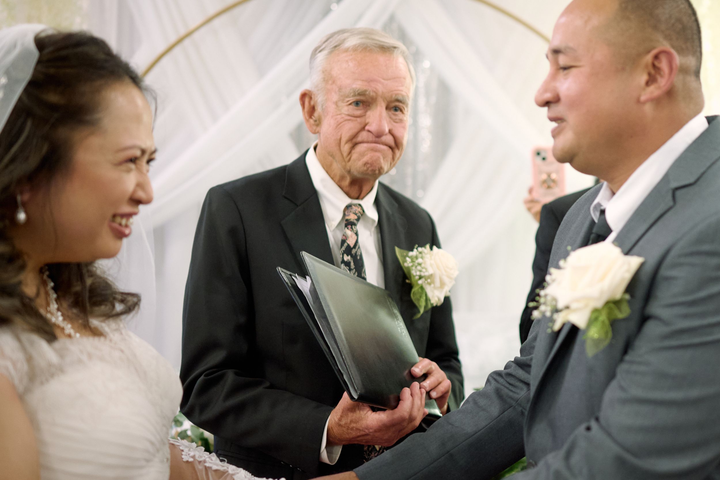 Wedding ceremony features an officiant with two boutonnieres joining the hands of a couple during their vows at Fairfield Inn & Suites Lodi.