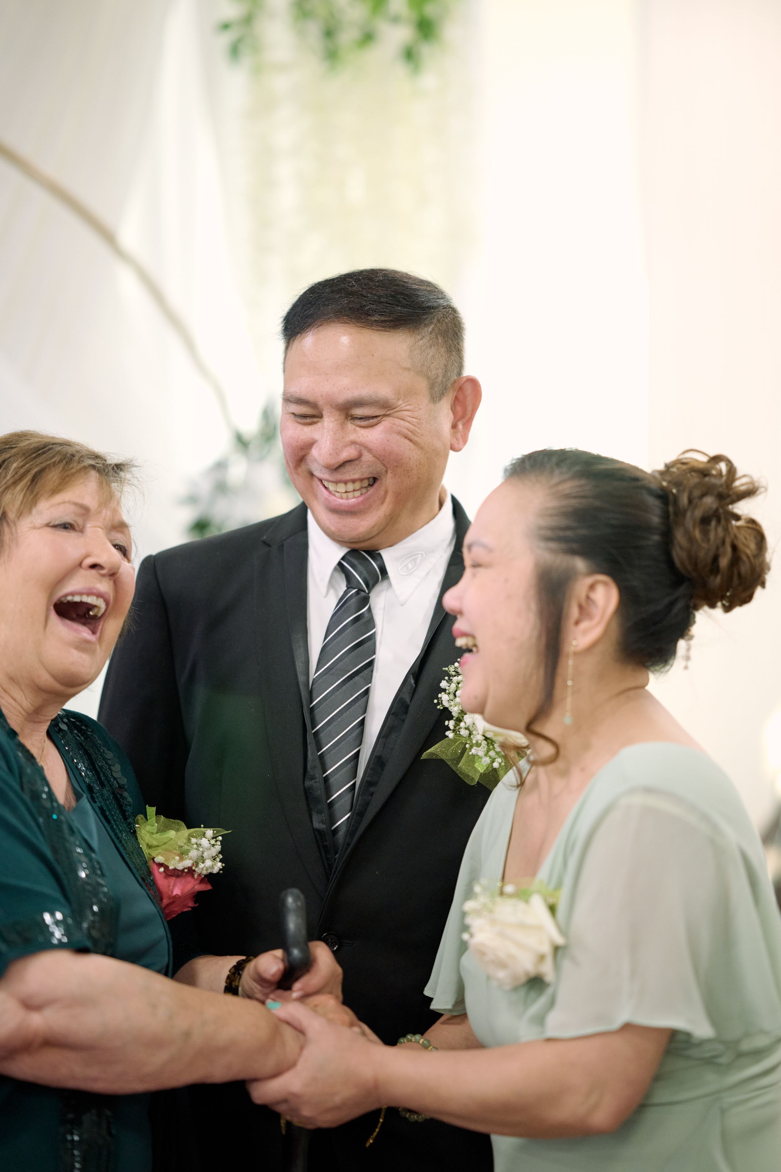 Group of three people share a heartfelt laugh together at a formal event, wearing corsages and dressy attire at Fairfield Inn & Suites CA.