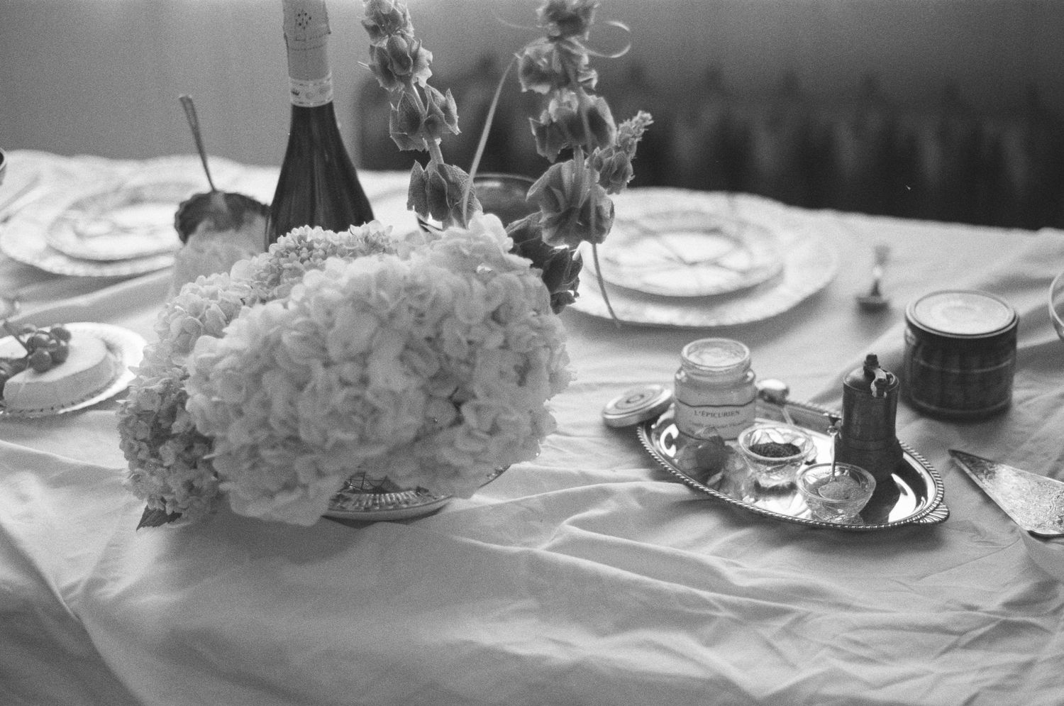 Elegant table setting with white hydrangeas, candles, and wine bottles in black and white.