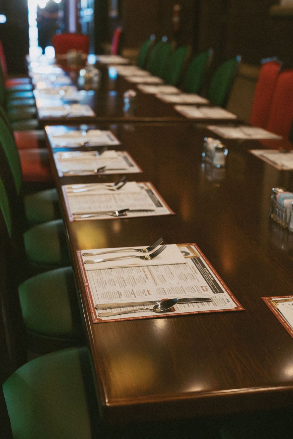 Long conference table set with multiple place settings and green chairs in a dimly lit room.