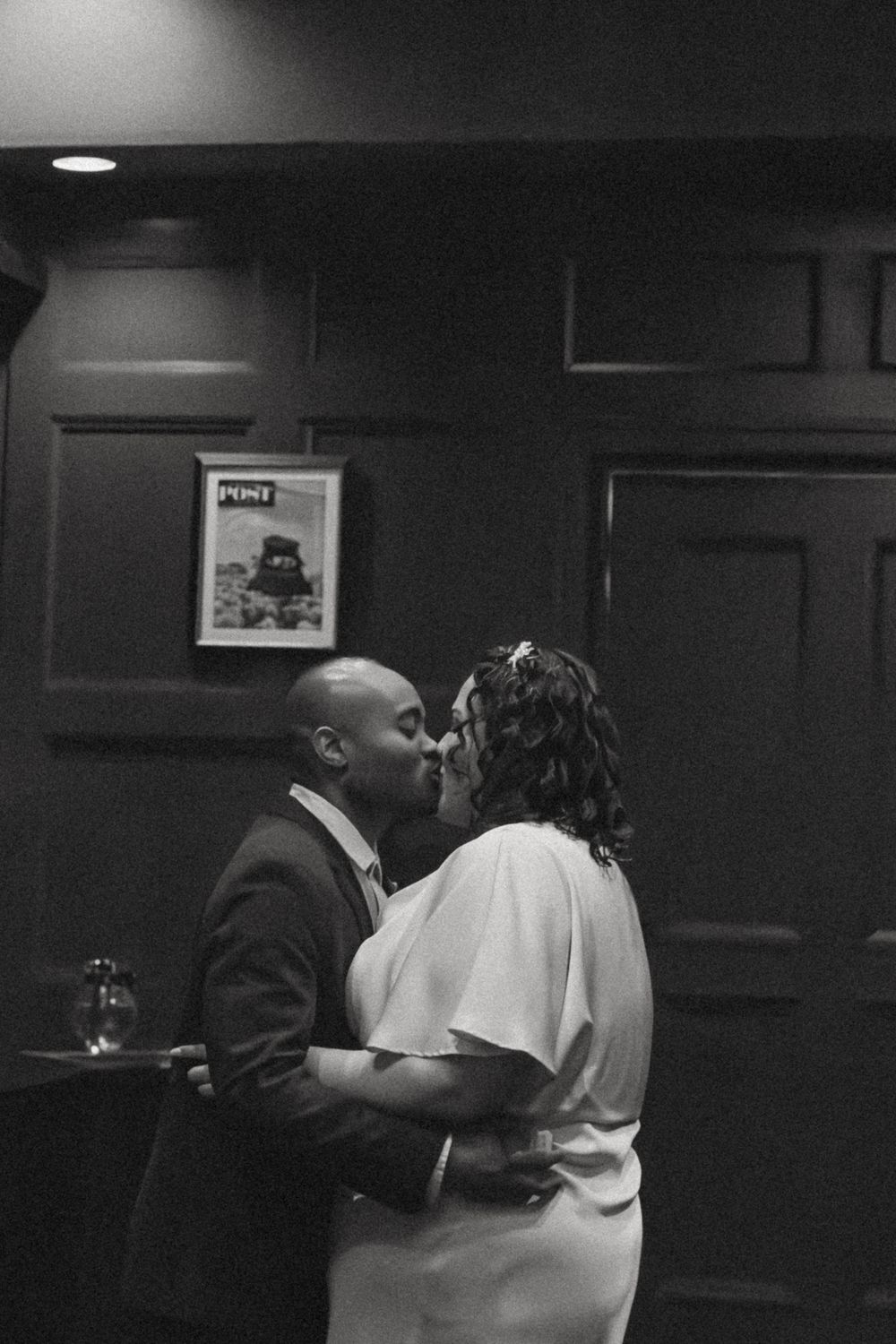 People embracing in a darkened room with moody lighting and wall decor.