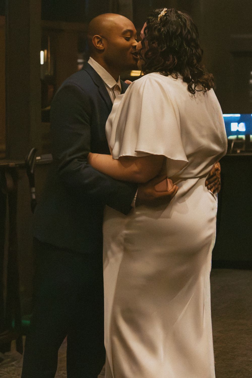Intimate moment captured in a dimly lit indoor space with formal attire.
