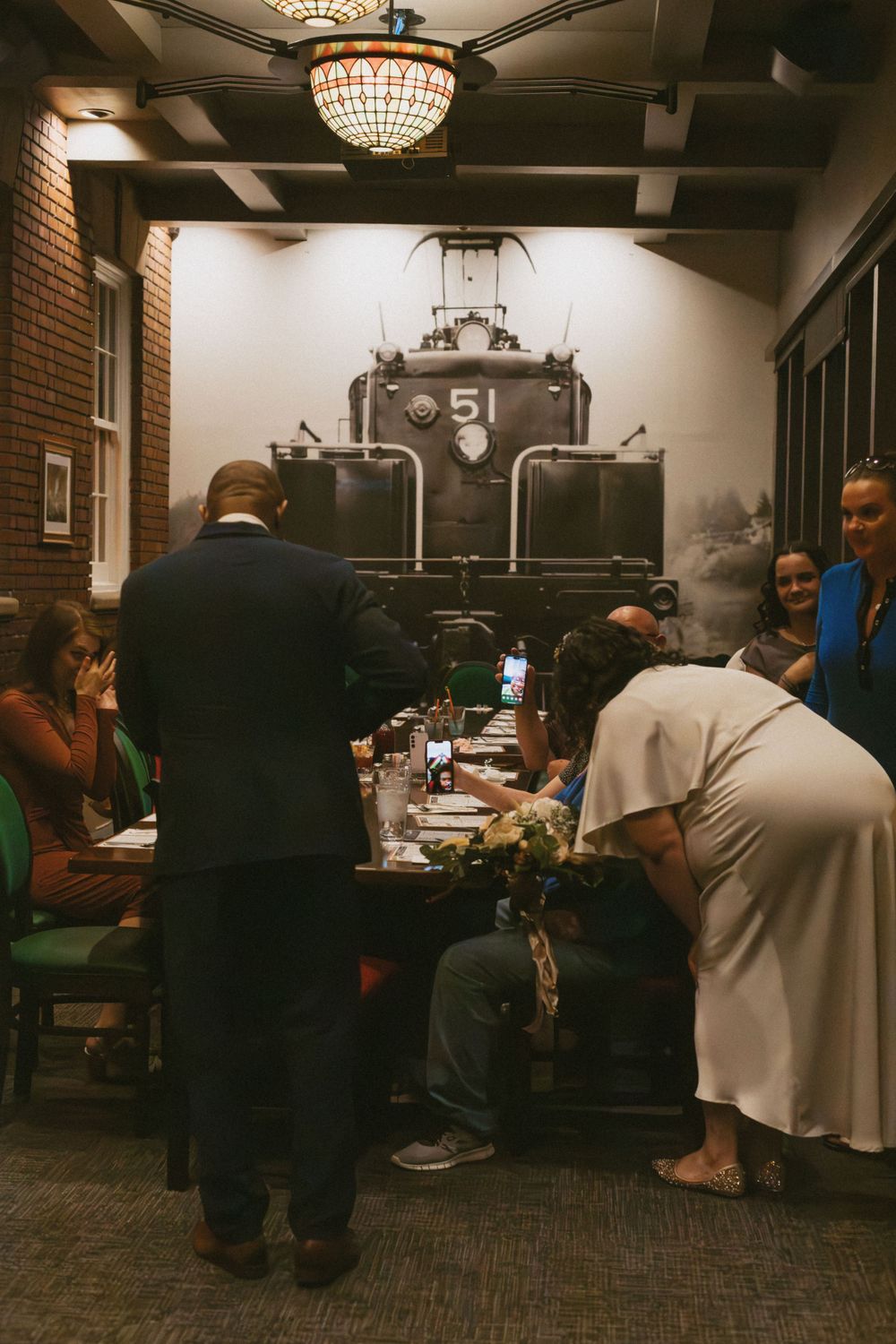 Social gathering in a brick-walled room with hanging chandeliers and casual seating.