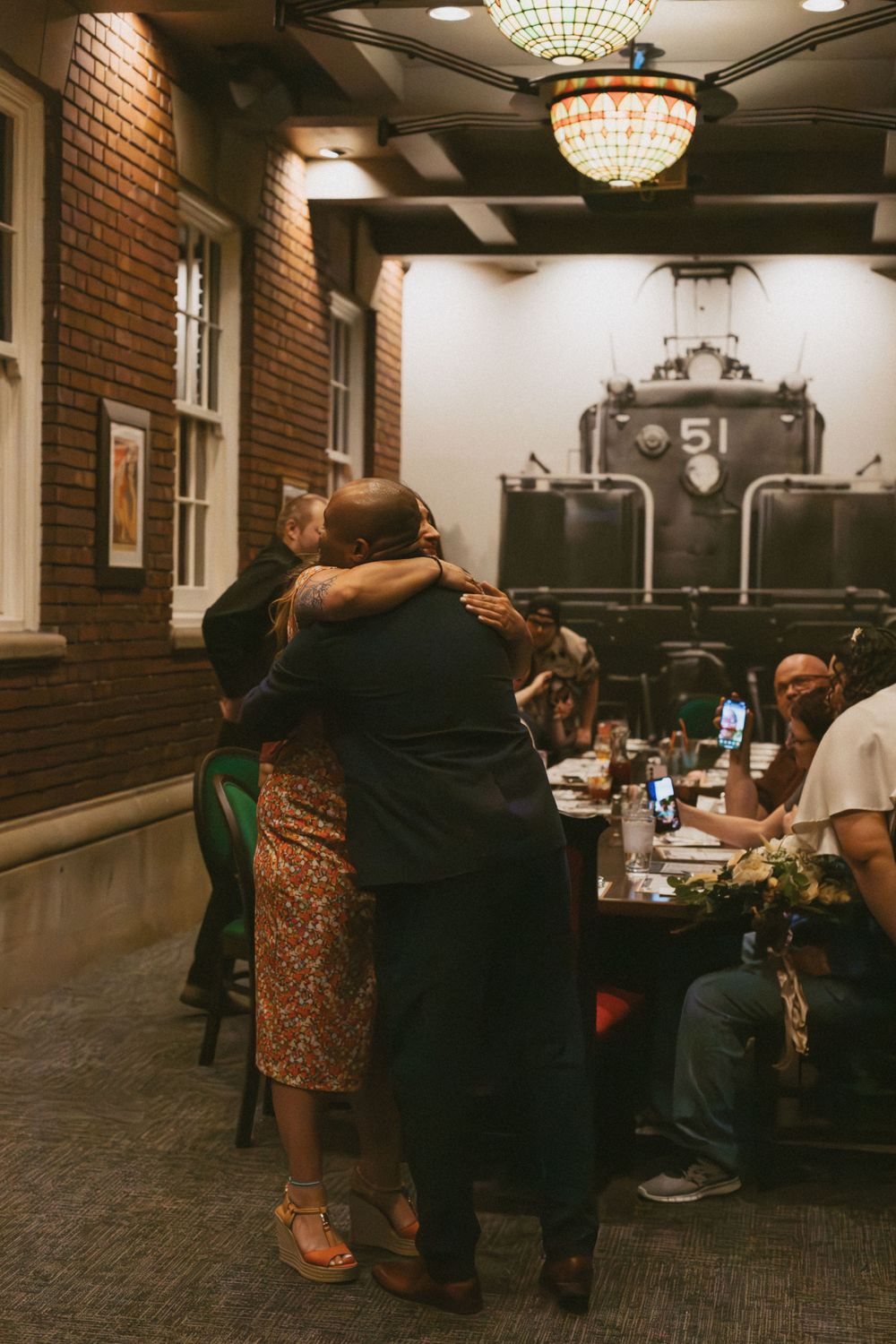 People mingling in a warmly lit room with exposed brick walls and elegant lighting fixtures.