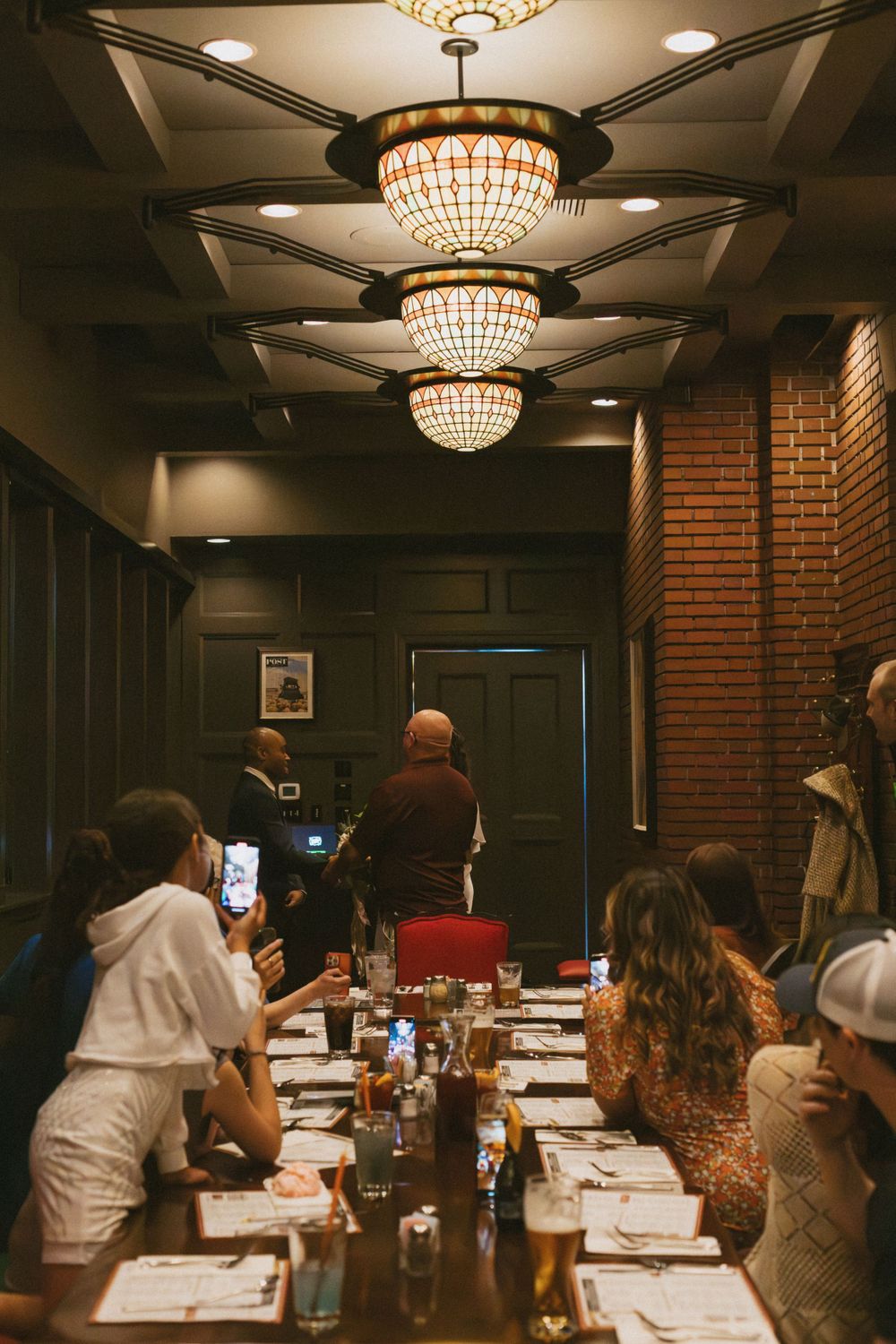 Elegant dining space with crystal chandeliers and exposed brick walls during an evening gathering.