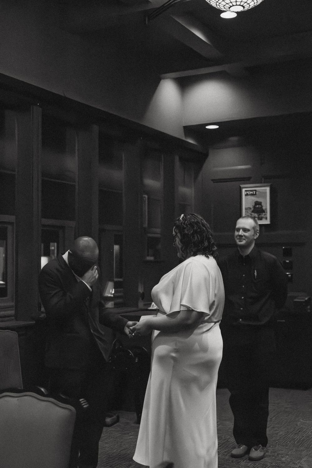 Dimly lit indoor gathering space with people embracing and interacting in formal attire.