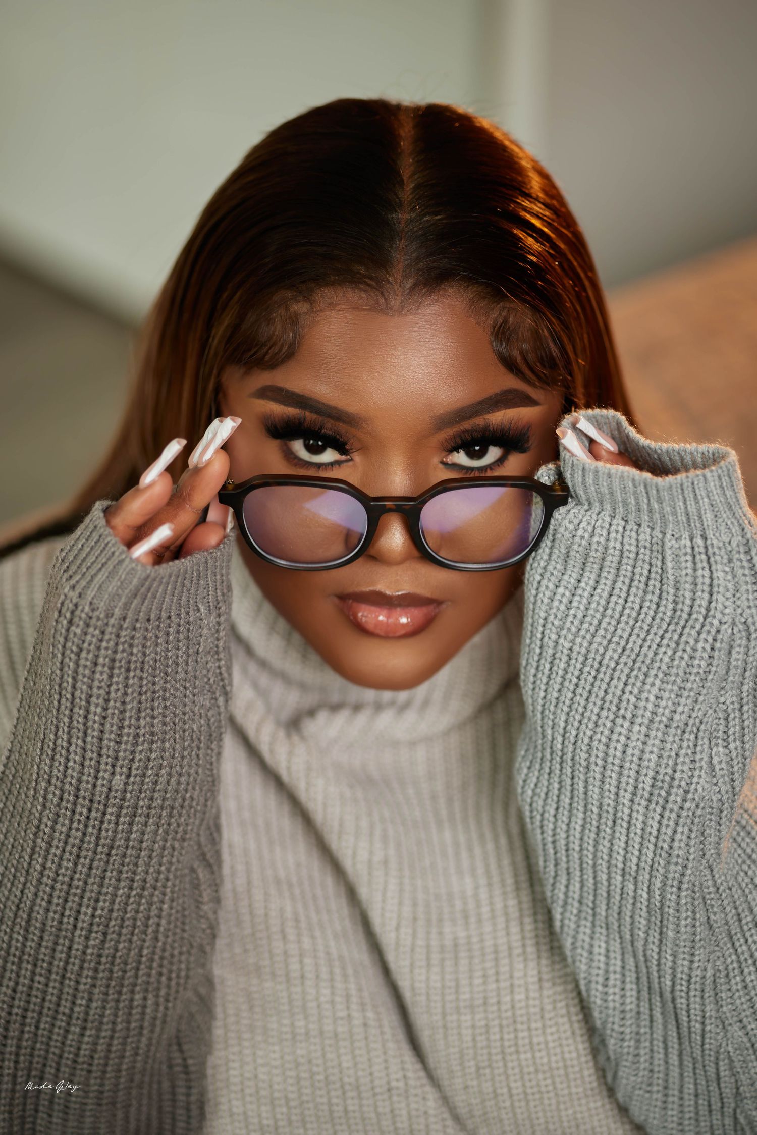 Portrait of person in cozy gray sweater adjusting glasses with manicured nails.