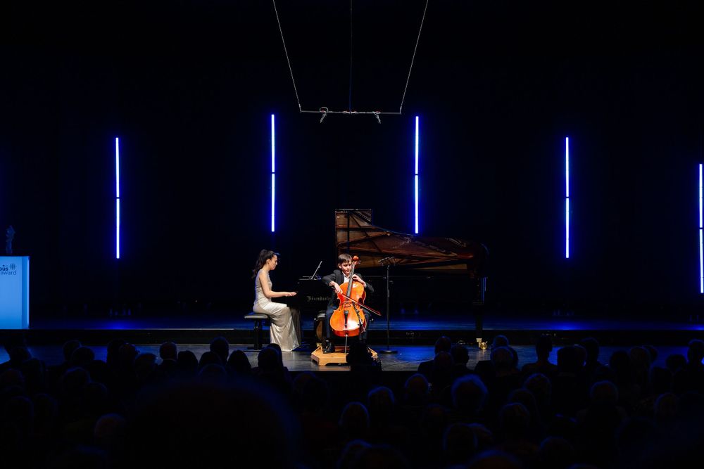Classical music duo performing with piano and cello under blue stage lights.