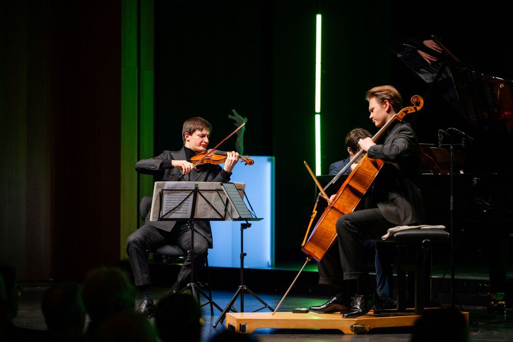 String musicians perform on stage with dramatic lighting and a blue digital display in the background.