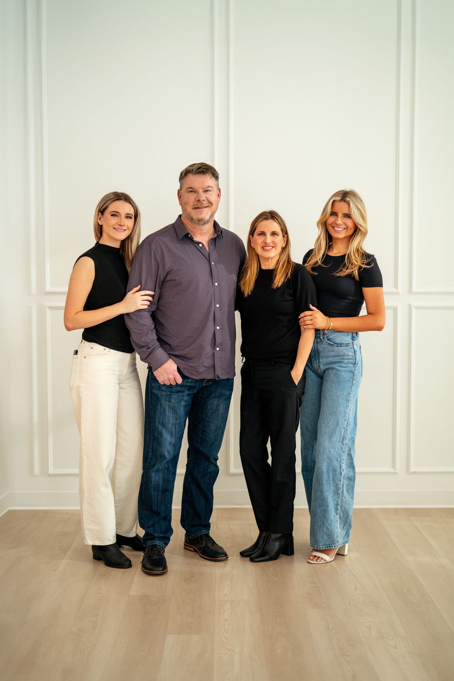Four people pose together in casual attire against a white paneled wall with minimalist modern decor.