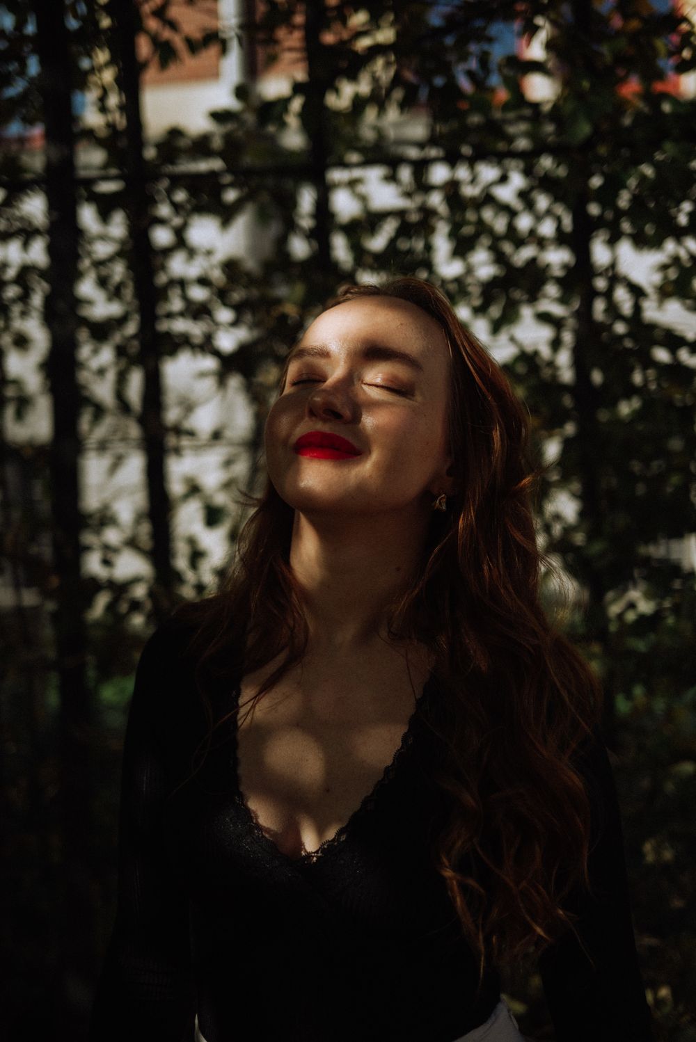 A close-up portrait of a woman with red lipstick, sunlight, and shadows on her face.