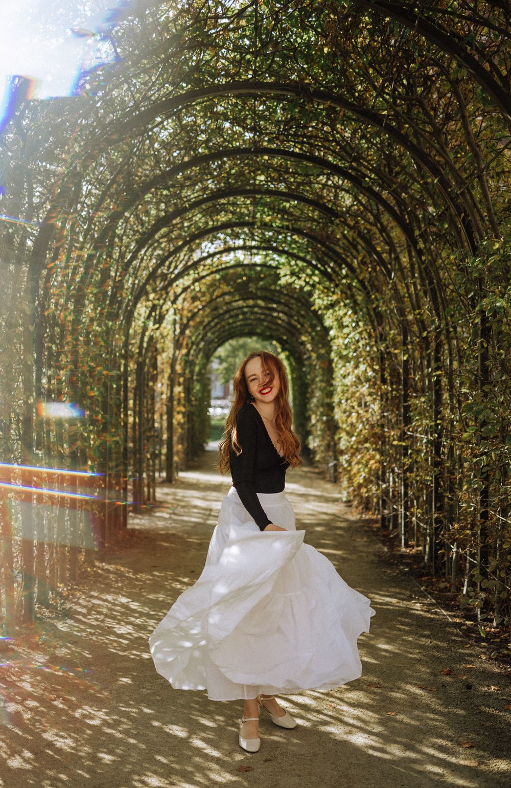 A red-haired woman in a white skirt spinning in a green archway in the gardens of the Rijksmuseum.