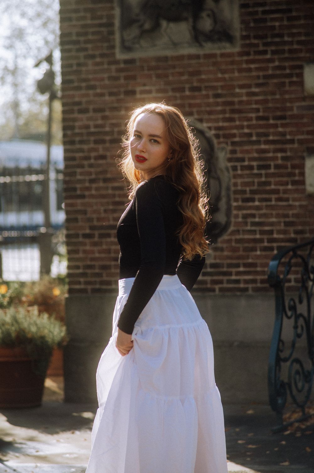Side profile of person in black turtleneck and white dress near brick wall.