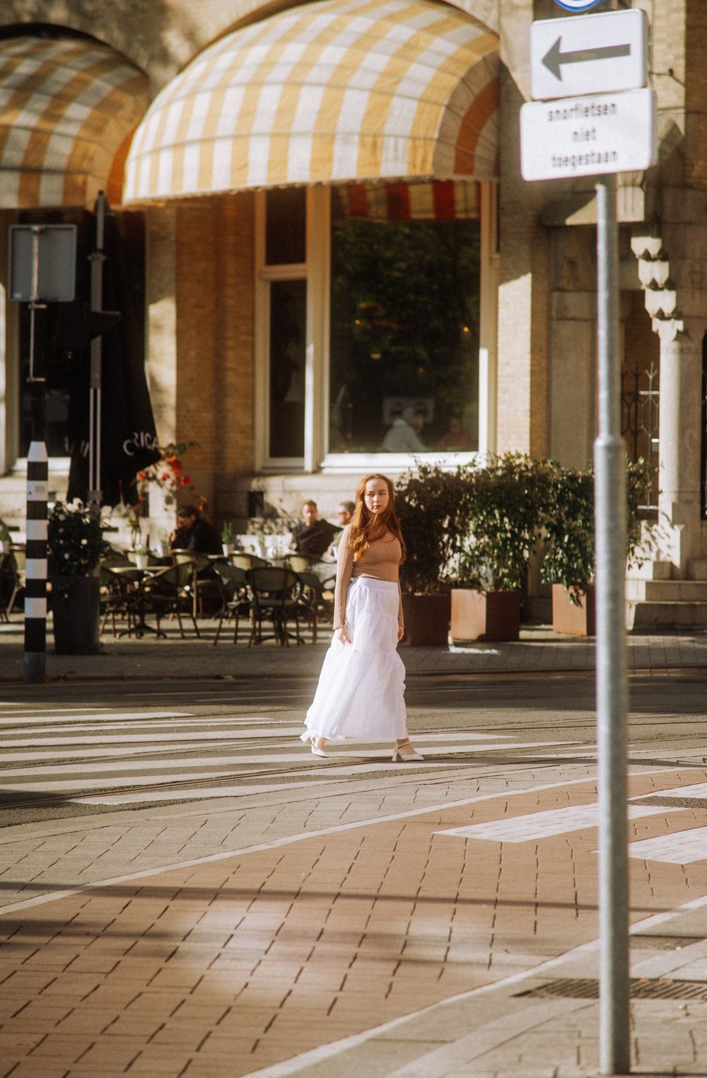 A figure in white moves gracefully under striped awnings in an urban courtyard.