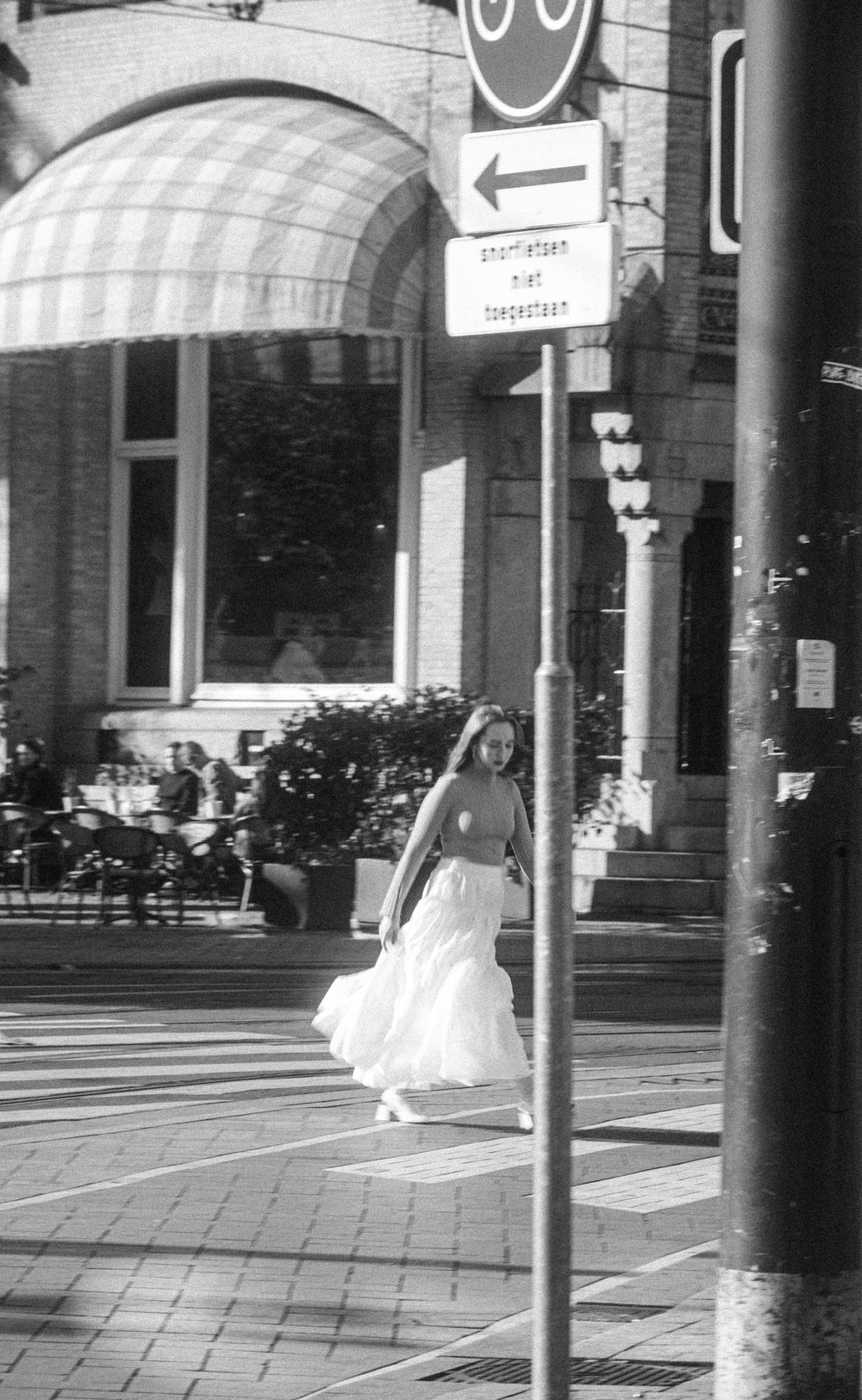 A person in white clothing moves through an urban space with striped awnings and street signs.