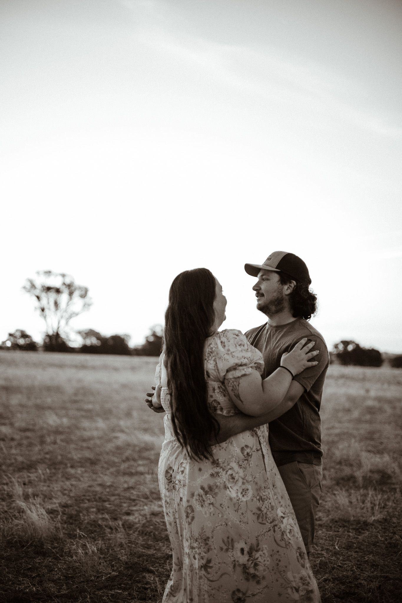 A romantic black and white portrait of a couple embracing in an open field at dusk.